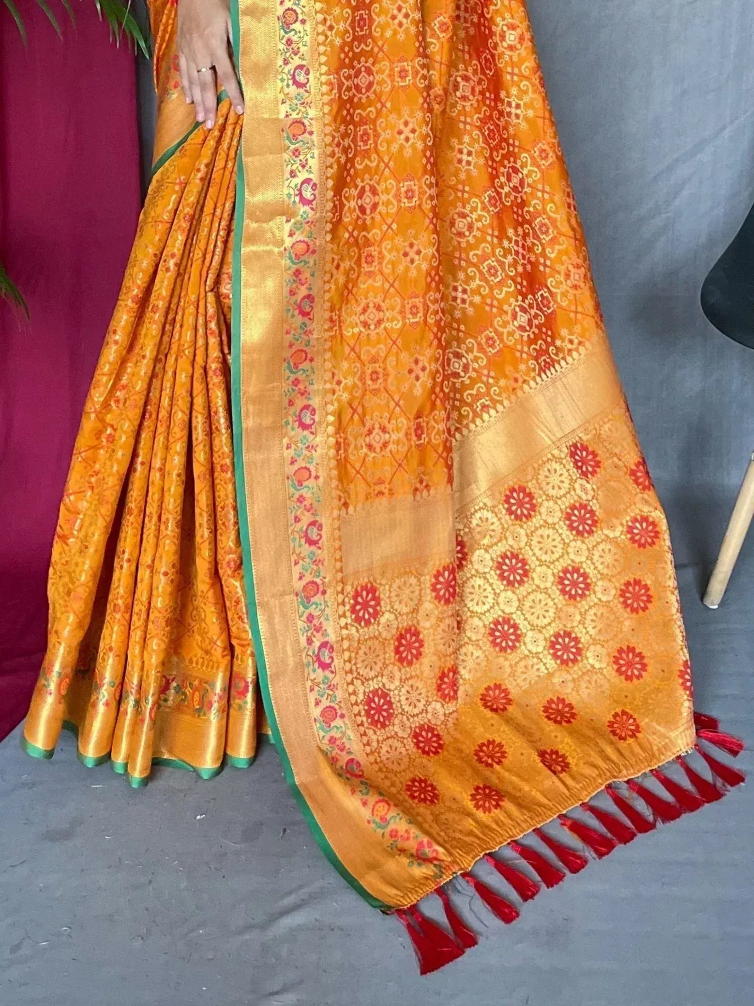 Vibrant orange designer saree with floral motifs, gold border, and red tassels, perfect for Indian ethnic wear.