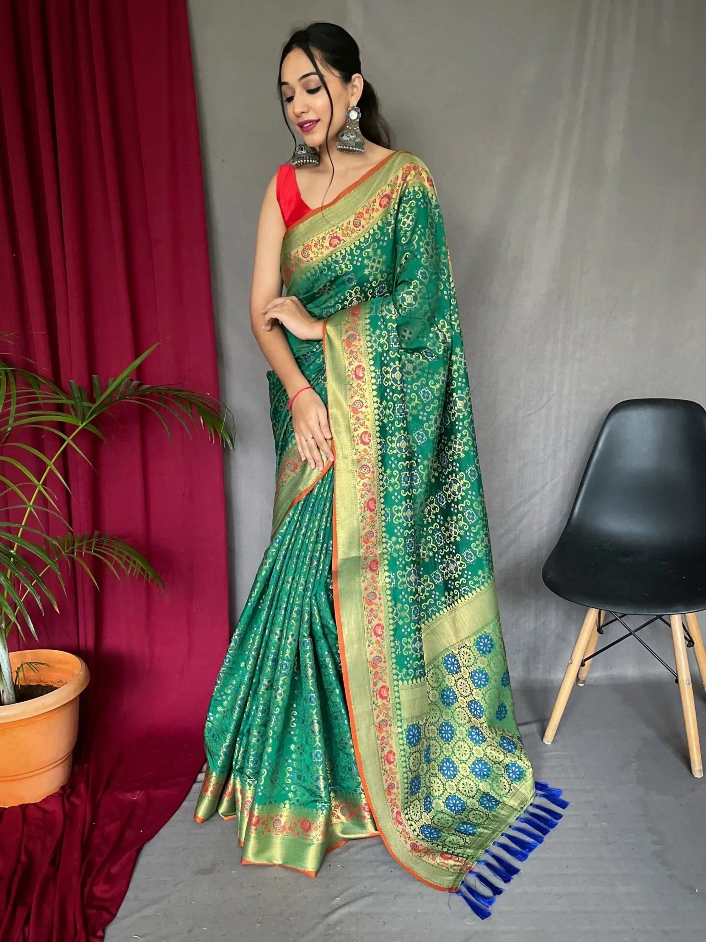 Woman in green printed saree with gold border and blue tassels, paired with red blouse and jhumka earrings
