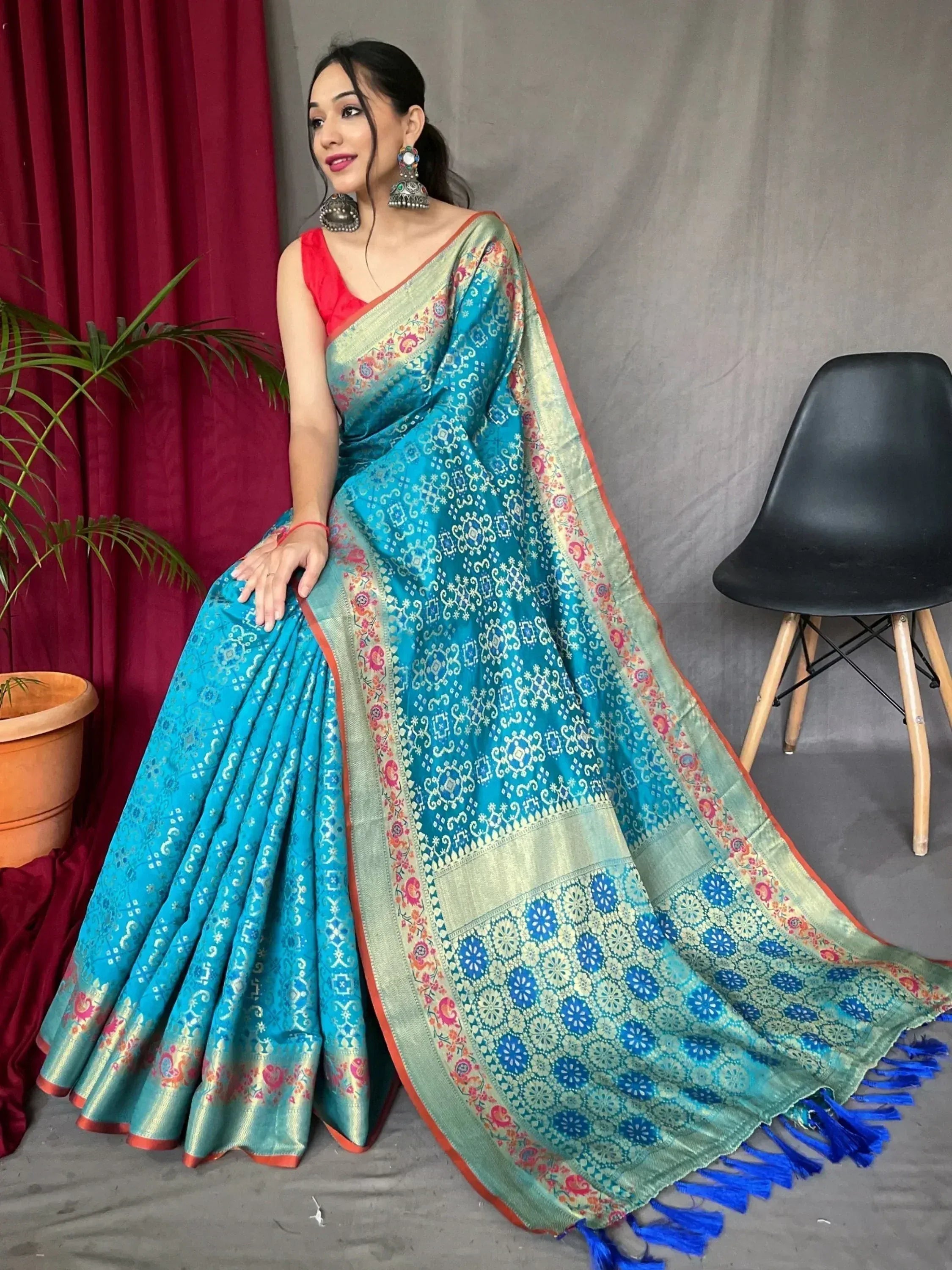 Woman in vibrant blue designer saree with floral border and tassels, paired with red blouse, showcasing Indian ethnic wear.