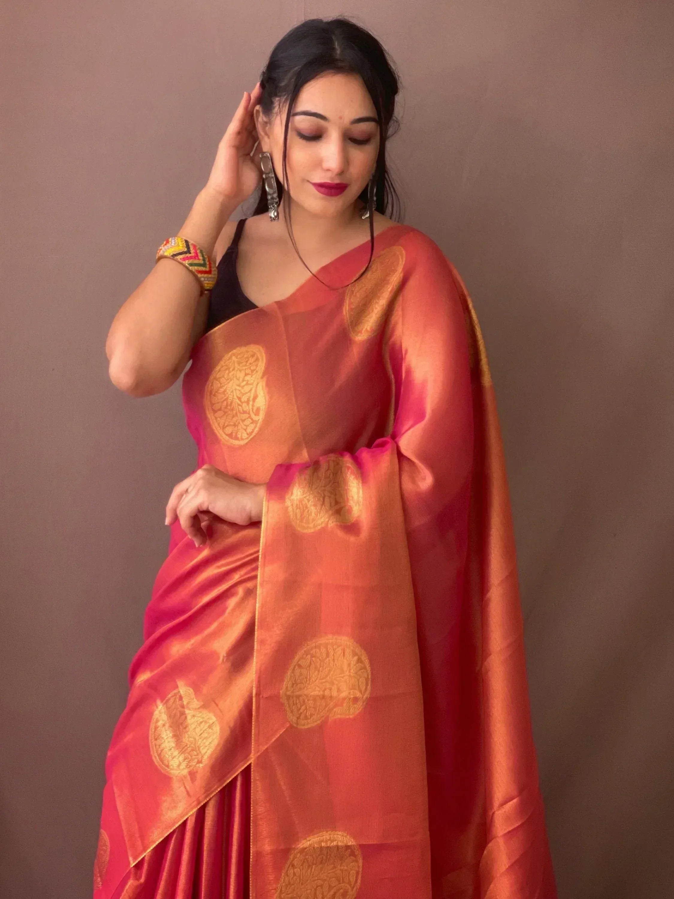 Woman in vibrant pink and orange saree with gold circular motifs, styled with ethnic jewelry for festive occasions