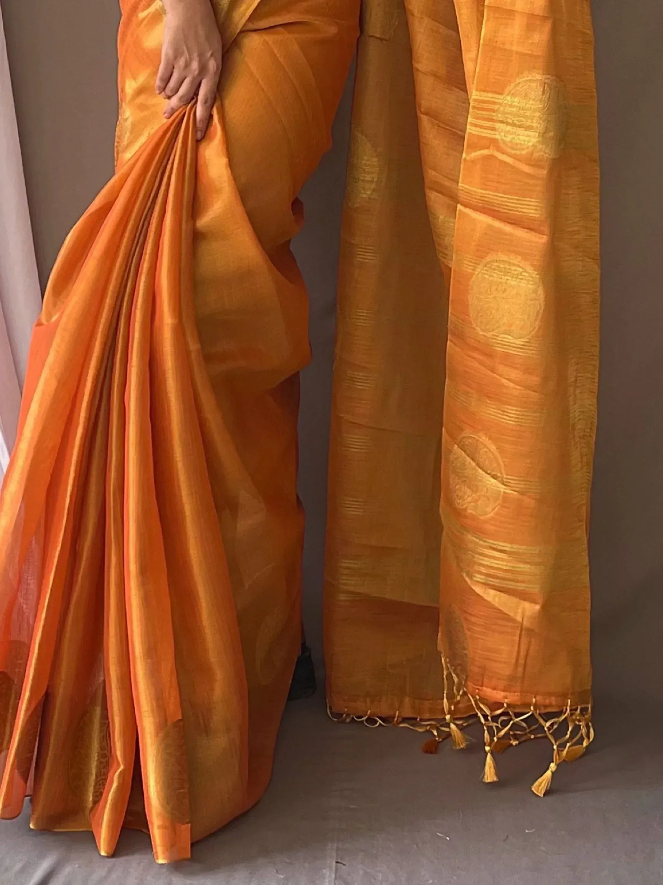 Vibrant orange Indian saree with gold woven motifs and tassels, showcasing ethnic wear design.