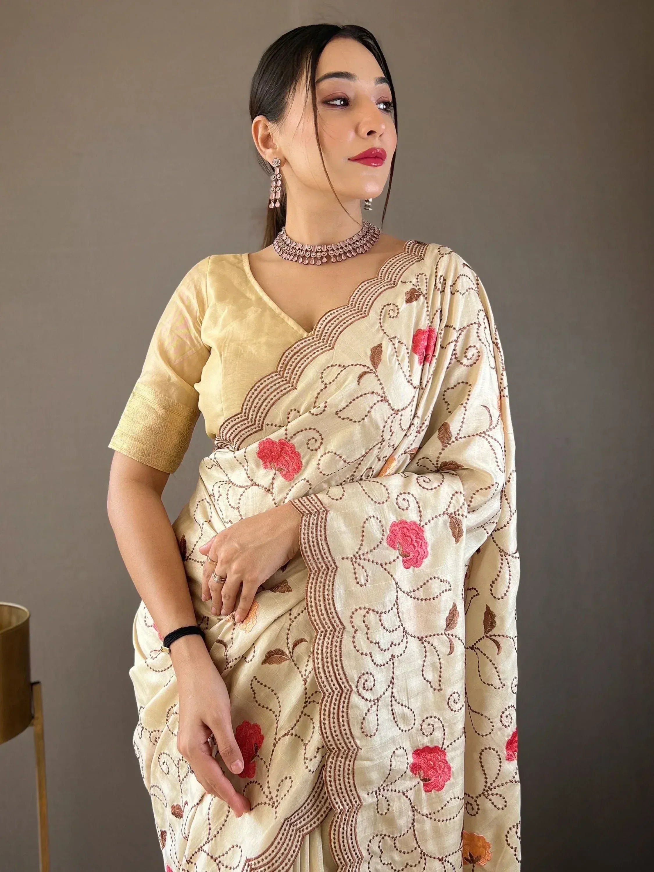 Cream saree with pink floral embroidery and gold blouse, styled with ethnic jewelry for Indian occasions