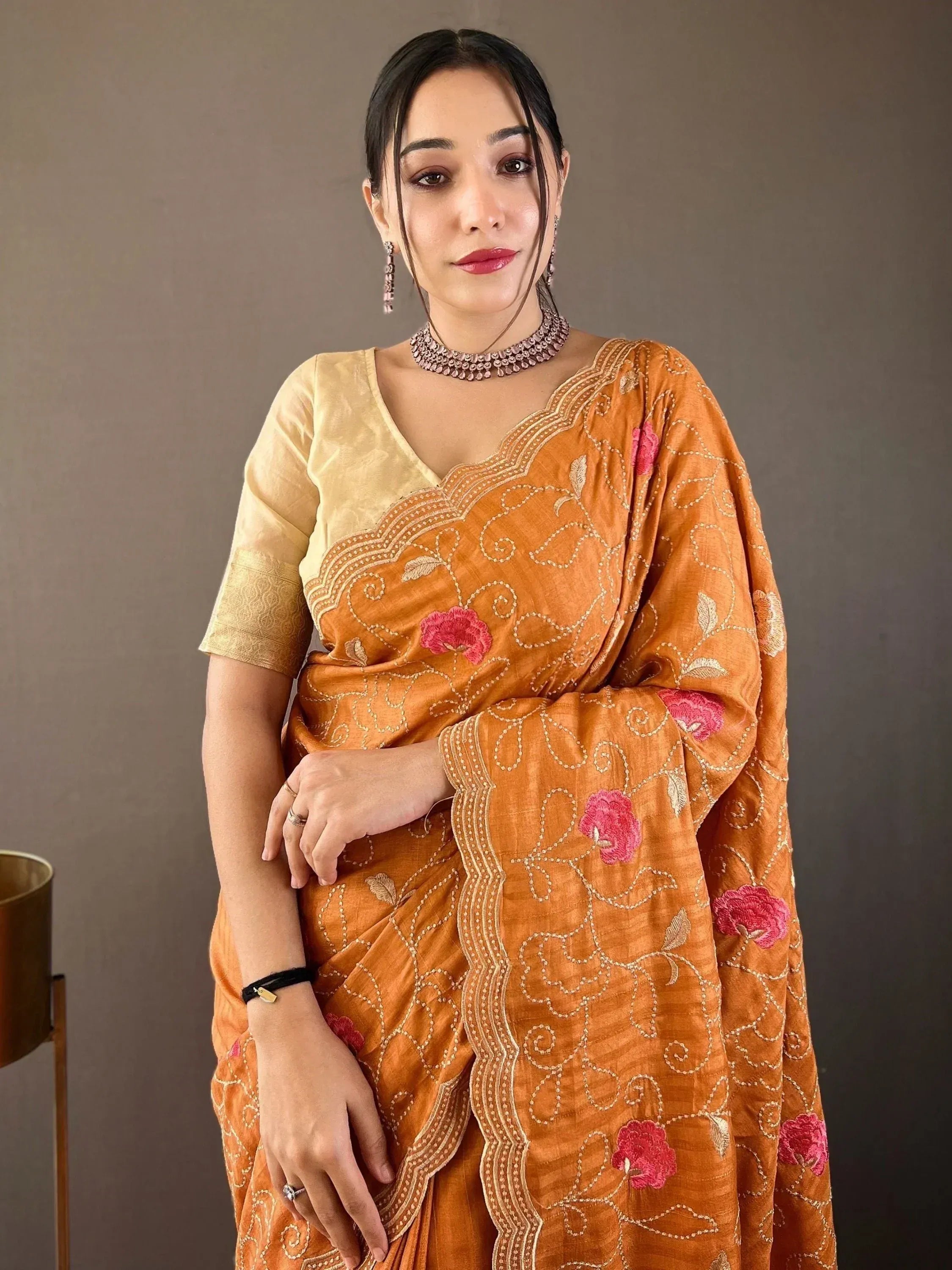 Woman in orange embroidered saree with pink floral motifs and gold blouse, styled with ethnic jewelry