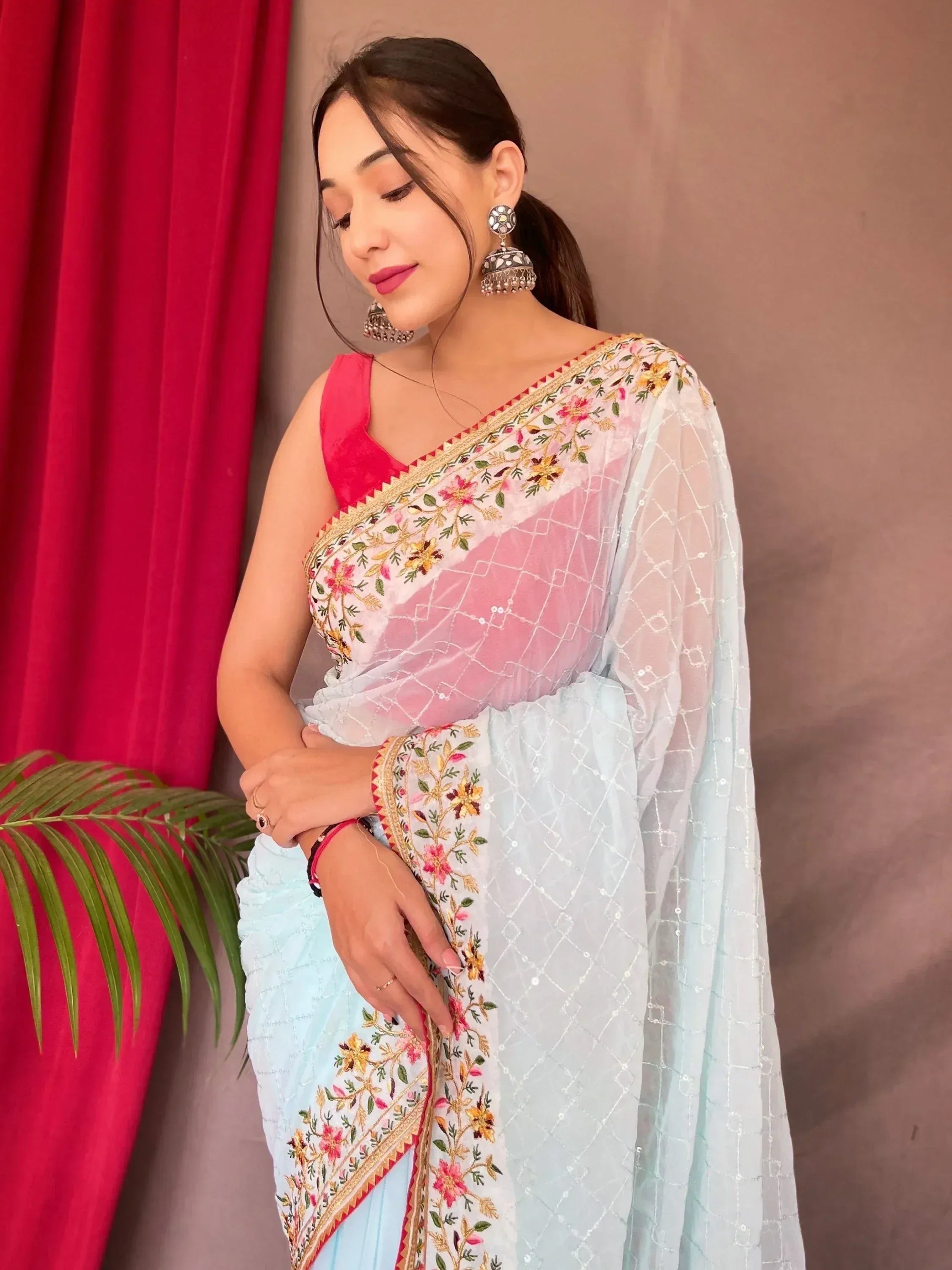 Woman in light blue embroidered saree with pink blouse and floral border, paired with jhumka earrings