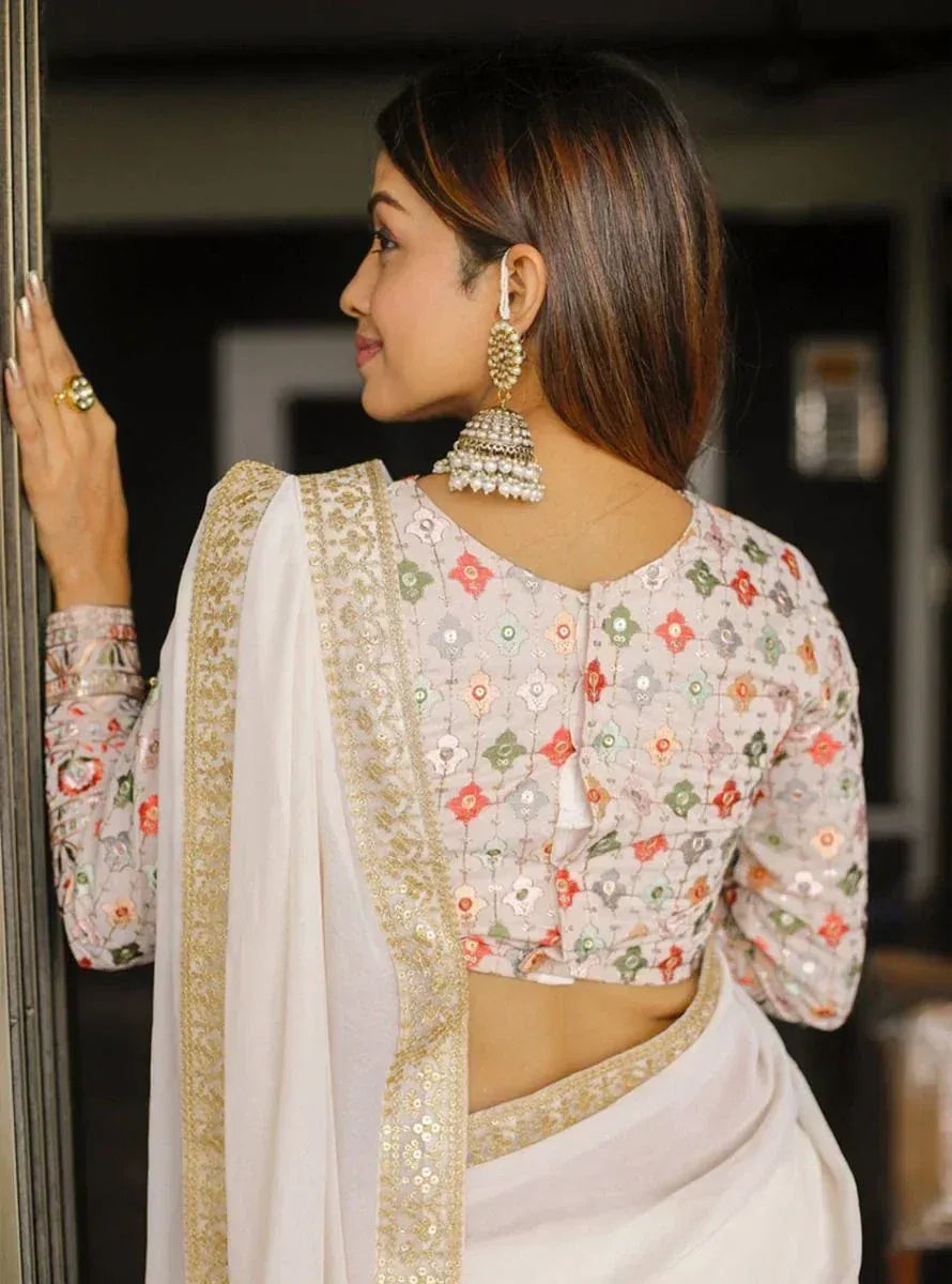 Woman in floral embroidered blouse with white saree and gold border, styled with jhumka earrings
