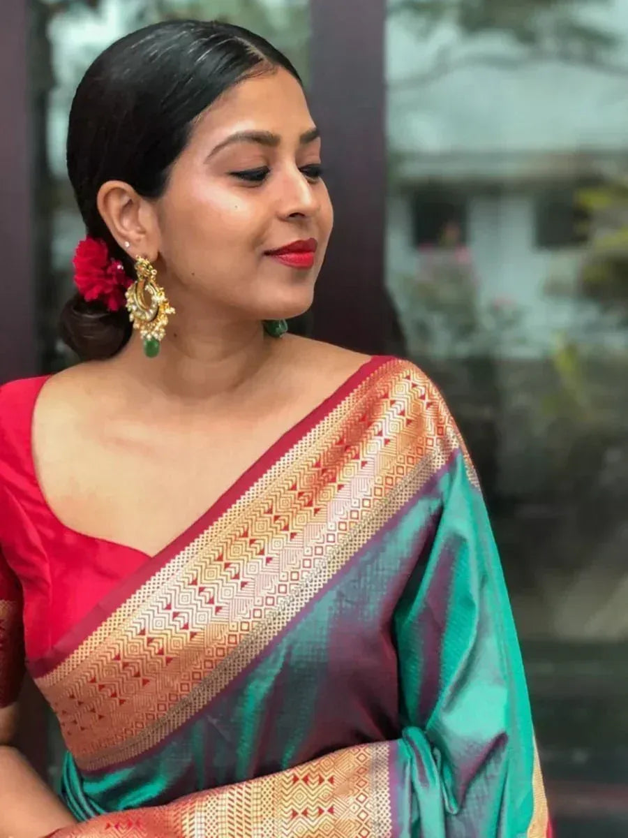 Woman in elegant teal and red saree with gold border, styled with floral hair accessory and jhumka earrings