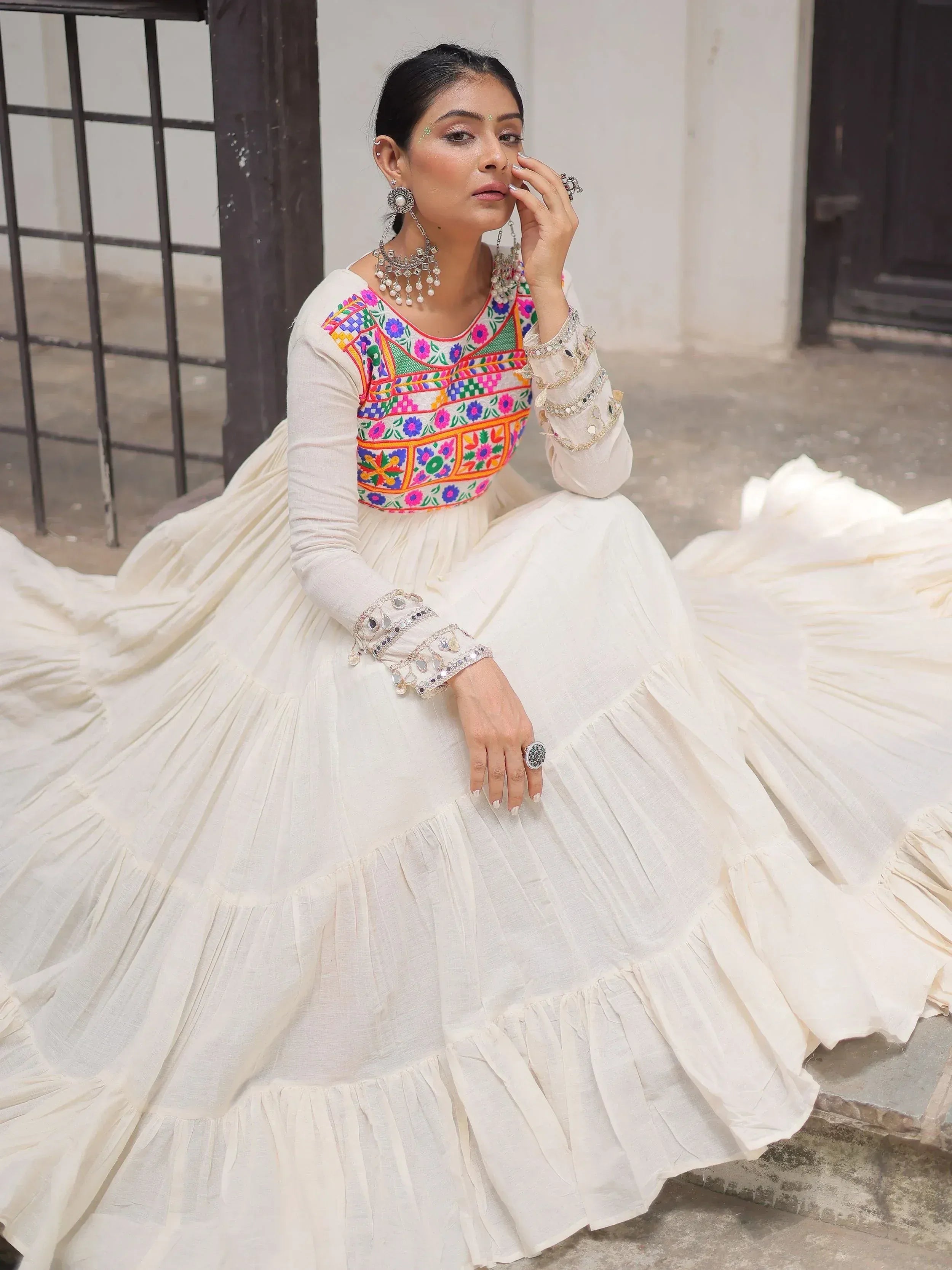 White ethnic gown with colorful floral embroidery and mirror work, styled with traditional jewelry