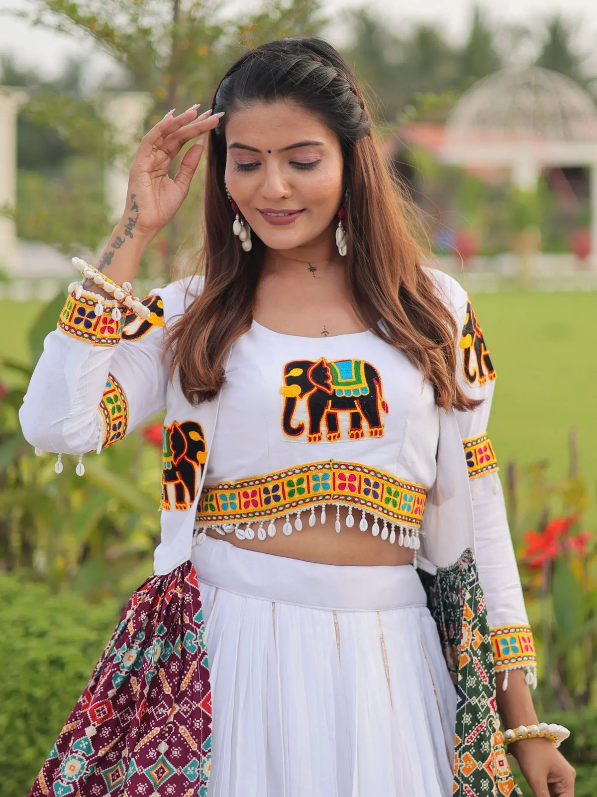 White ethnic crop top with elephant embroidery and colorful mirror work, paired with pleated skirt for festive wear