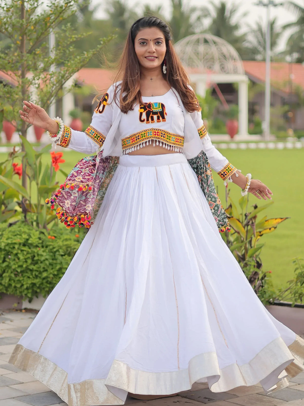 White ethnic lehenga choli with elephant embroidery, colorful mirror work, and pom-pom dupatta for festive occasions