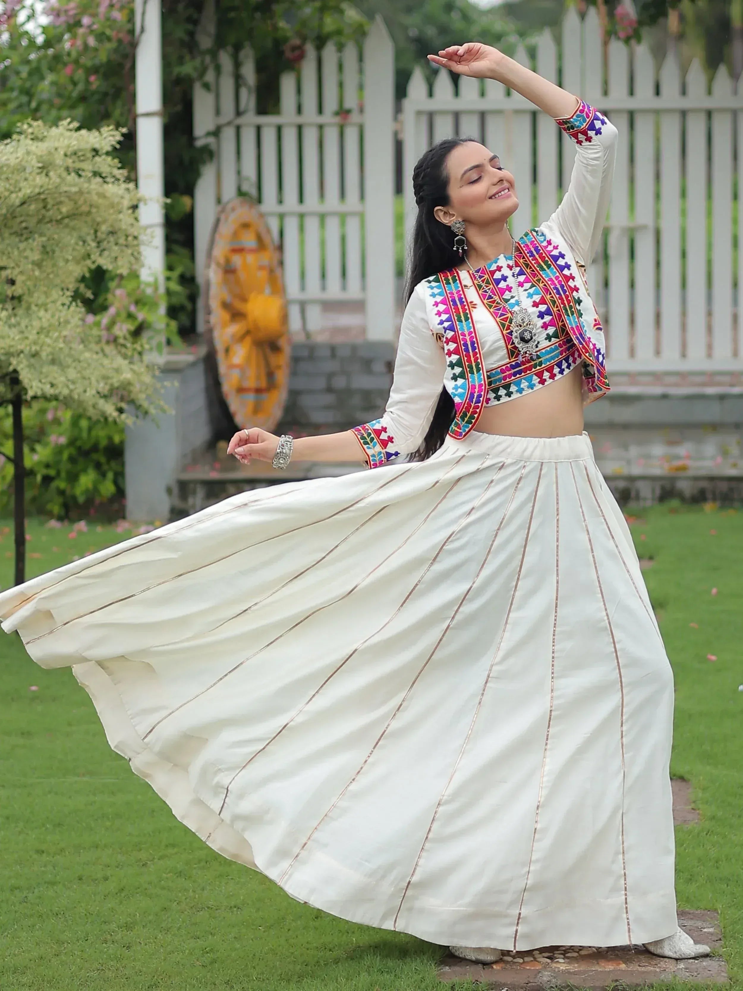 Woman in white embroidered lehenga choli twirling in garden, colorful ethnic wear