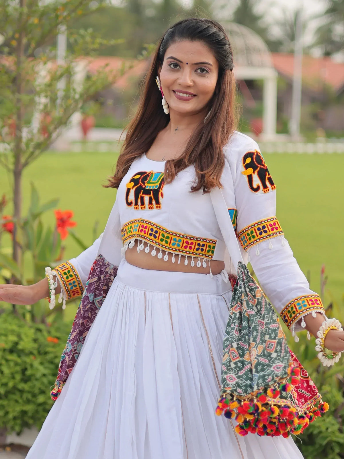 White ethnic crop top with elephant embroidery and colorful mirror work, paired with pleated skirt and dupatta, perfect for Indian festive wear.