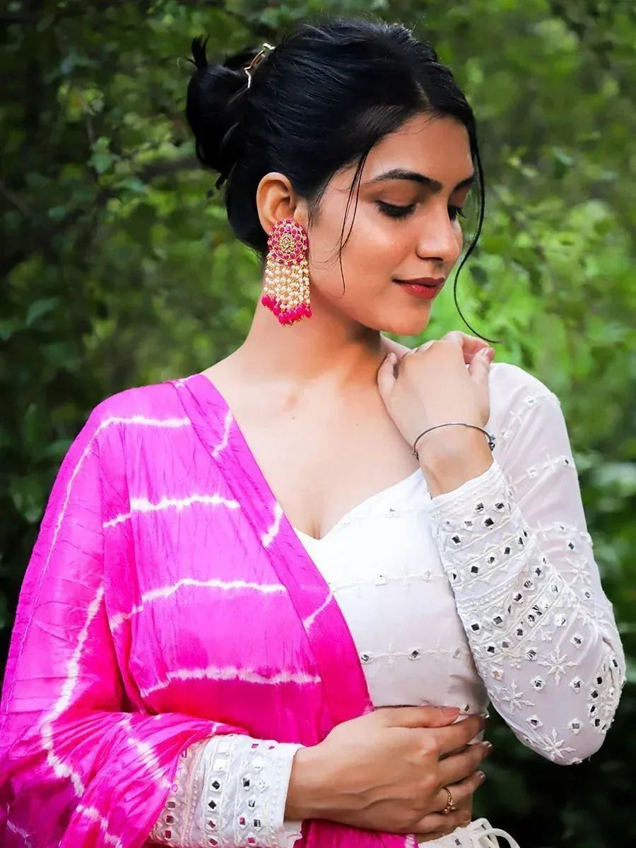 Woman in white embroidered kurta with pink tie-dye dupatta, wearing statement earrings, perfect for ethnic occasions.