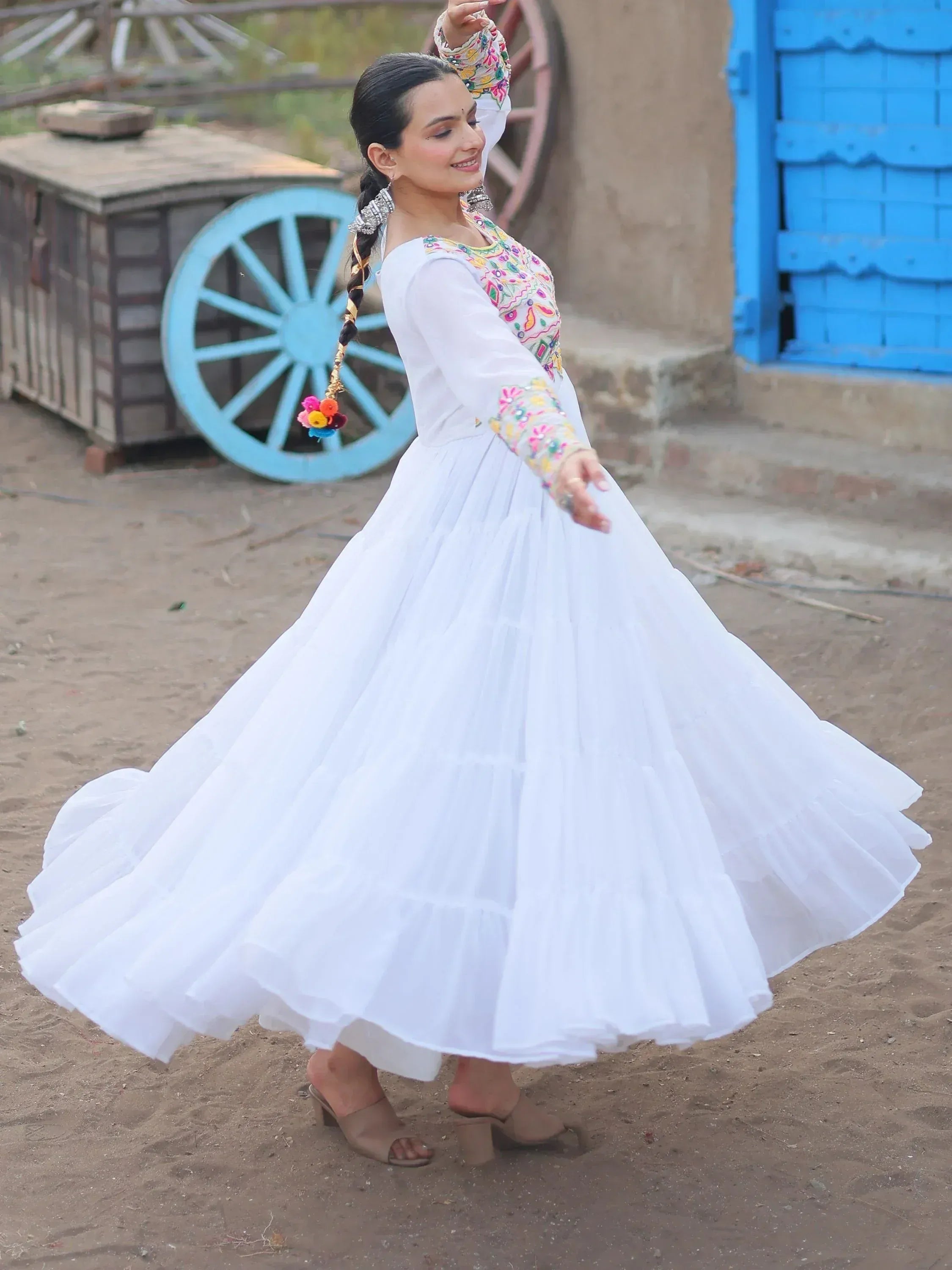 Woman in white embroidered ethnic gown with flared skirt, dancing near blue cart and door