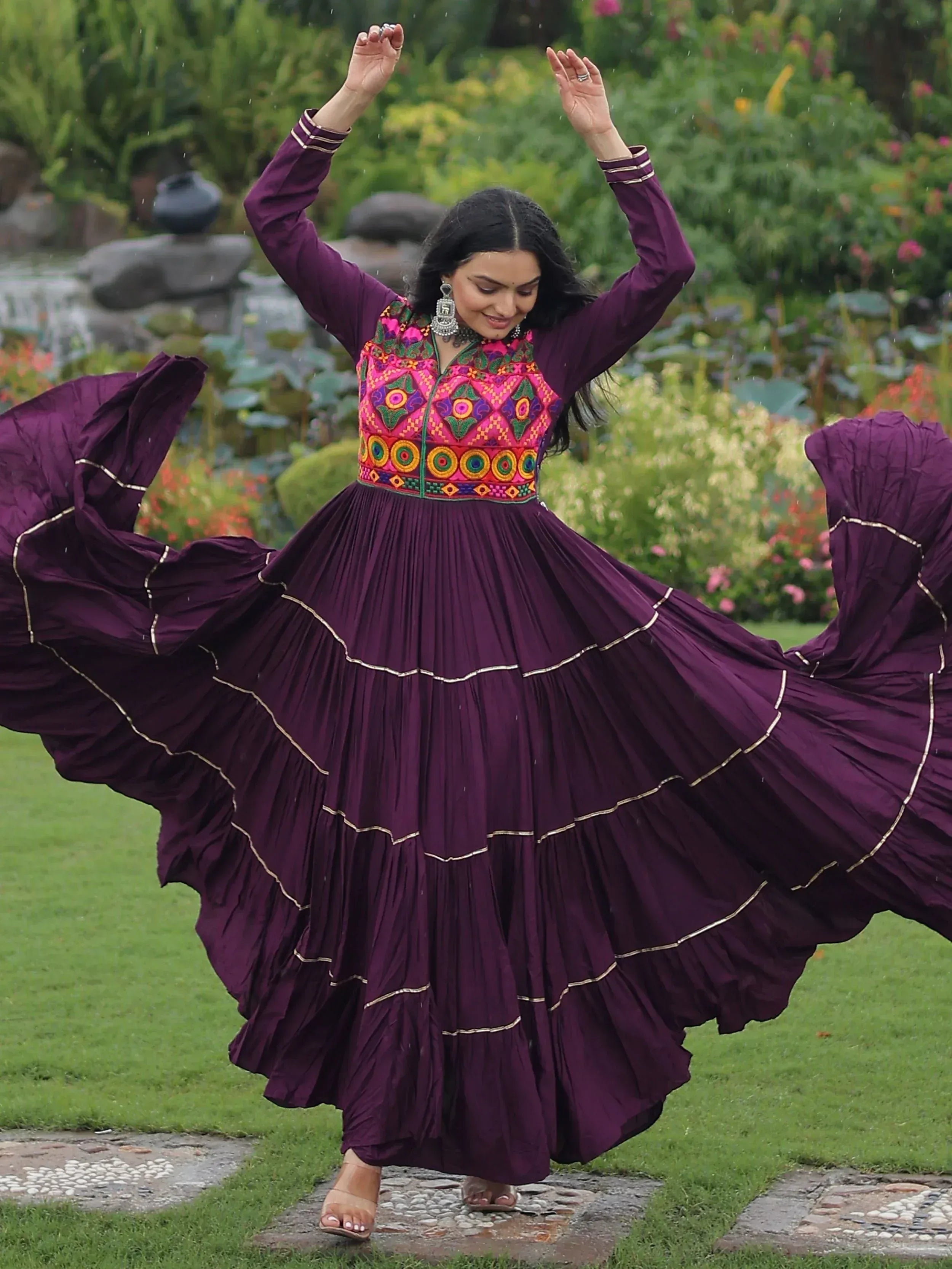 Woman twirling in purple ethnic gown with colorful embroidery, garden setting