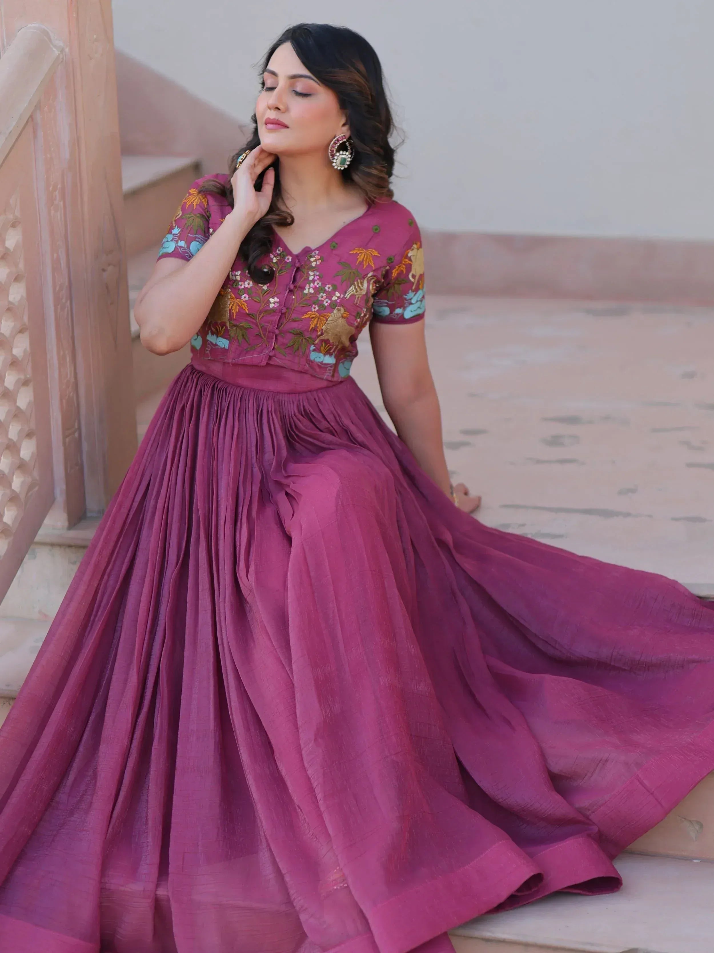 Woman in maroon embroidered ethnic gown with floral motifs, perfect for Indian occasions and celebrations.