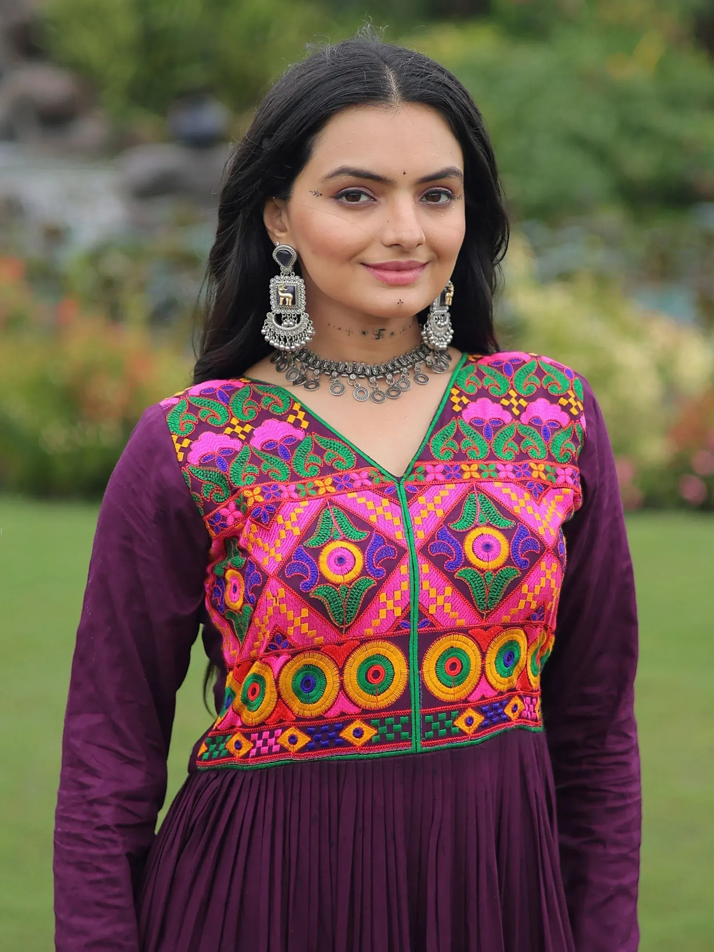 Woman in vibrant purple ethnic gown with colorful floral embroidery, traditional jewelry, garden setting