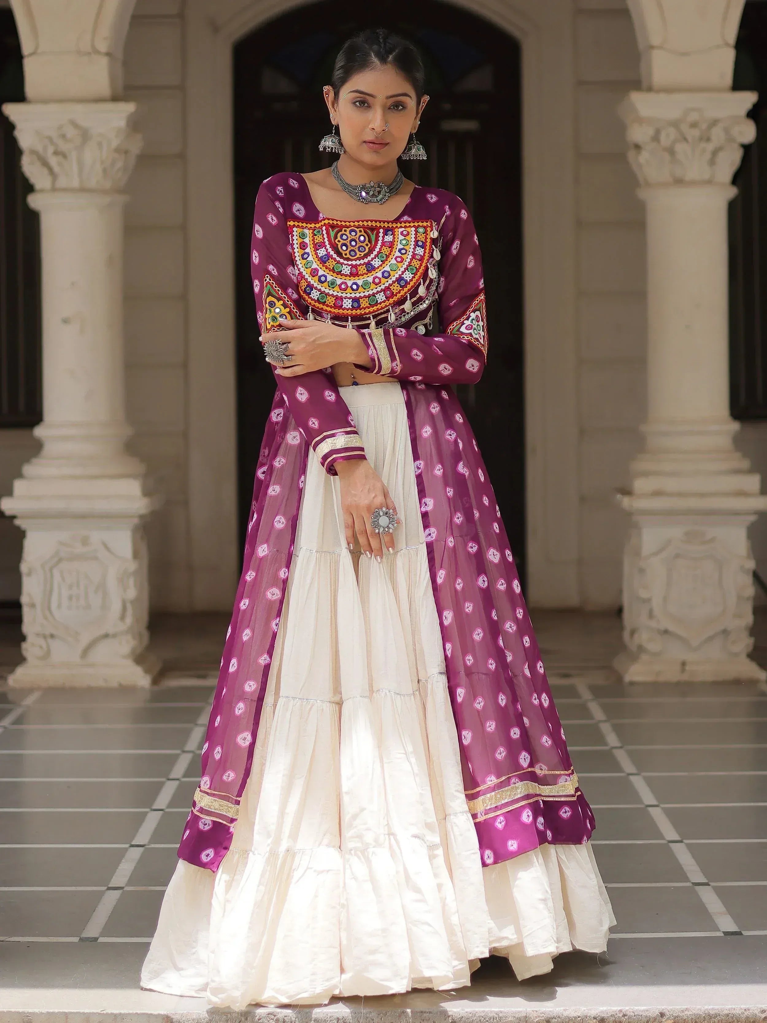 Woman in purple and cream ethnic lehenga choli with mirror work, standing at palace entrance