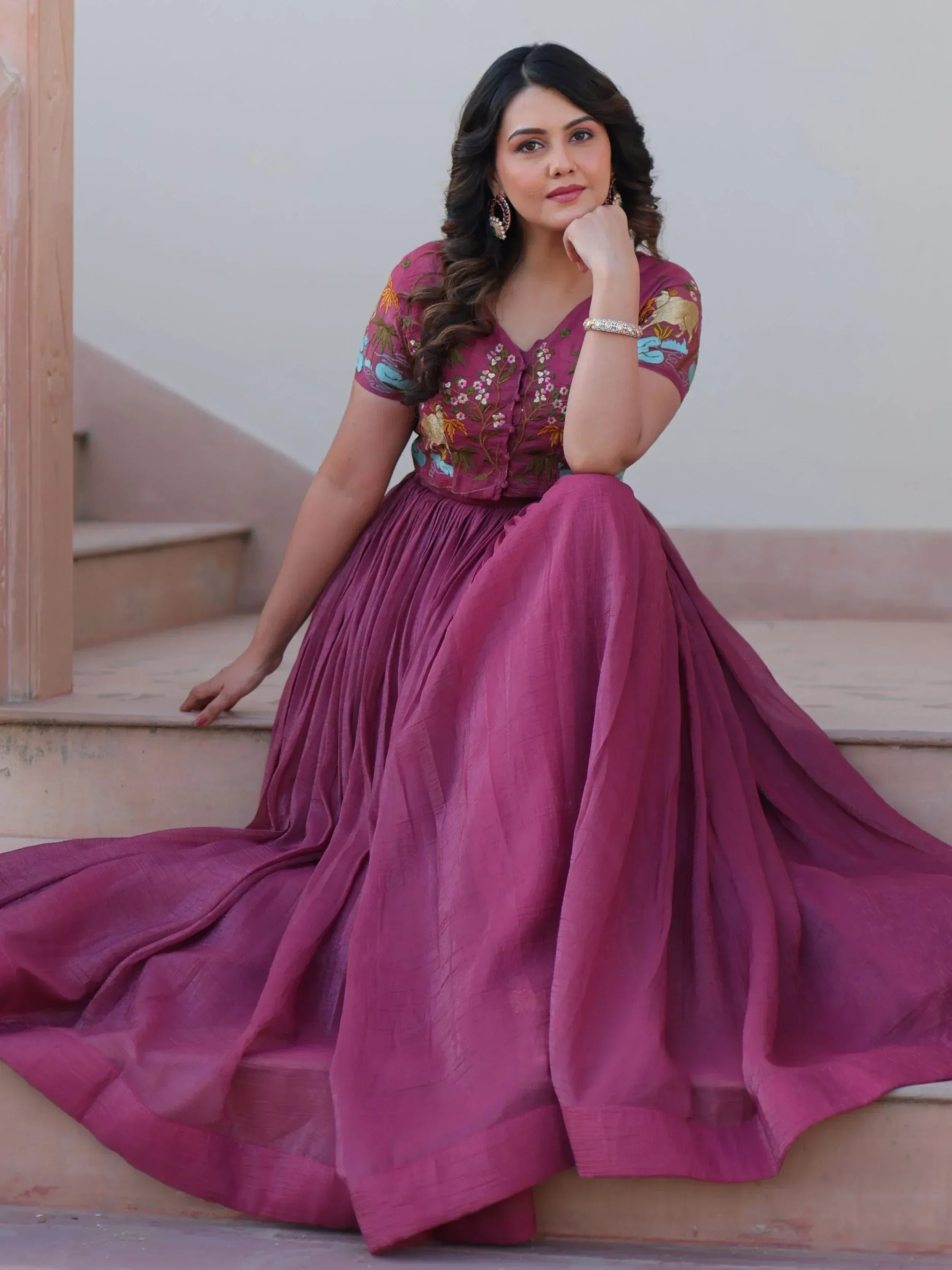 Woman in maroon embroidered ethnic gown with floral motifs, sitting on stairs