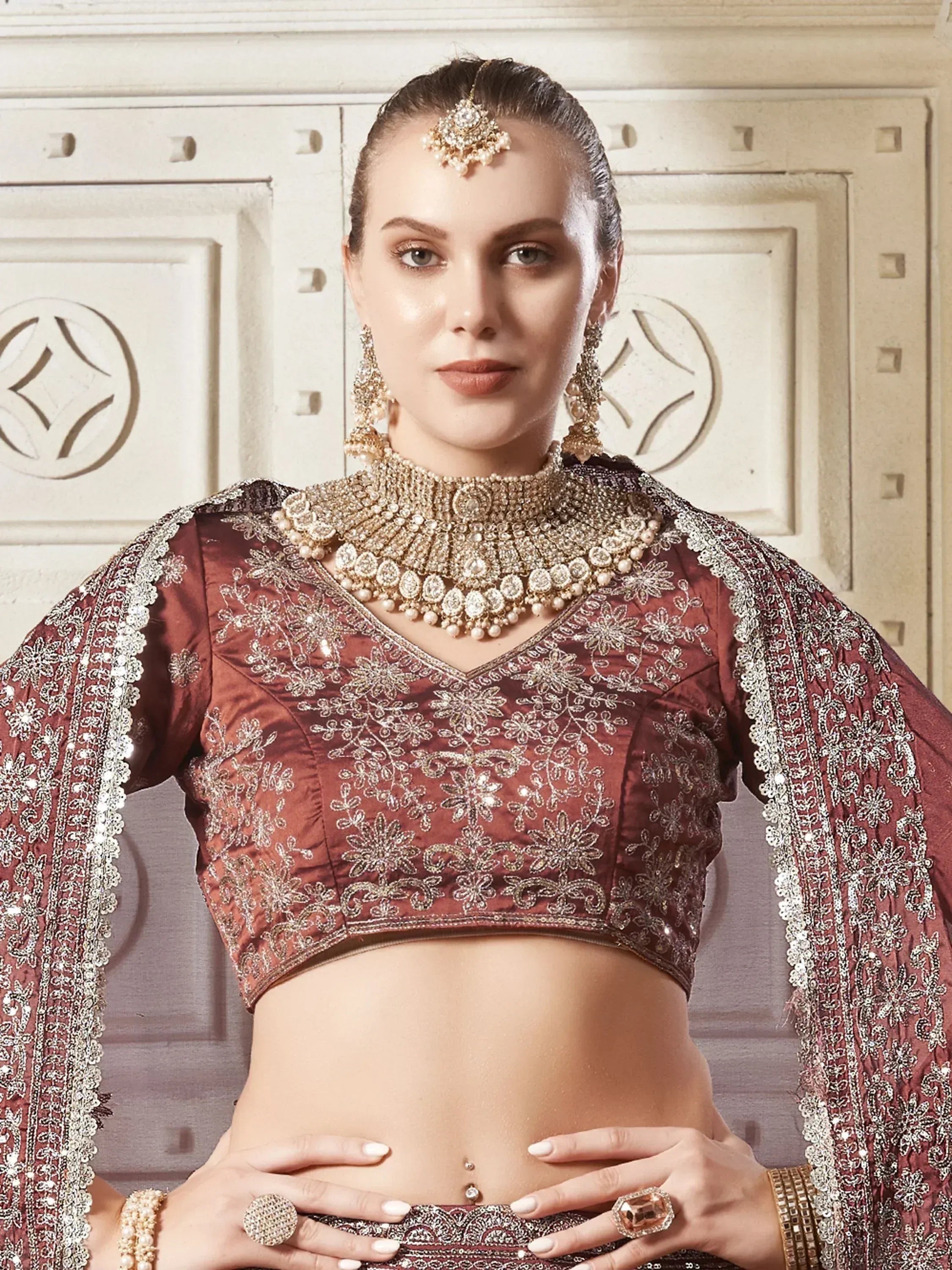 Elegant maroon embroidered lehenga choli with heavy gold jewelry, perfect for Indian weddings and festive occasions.