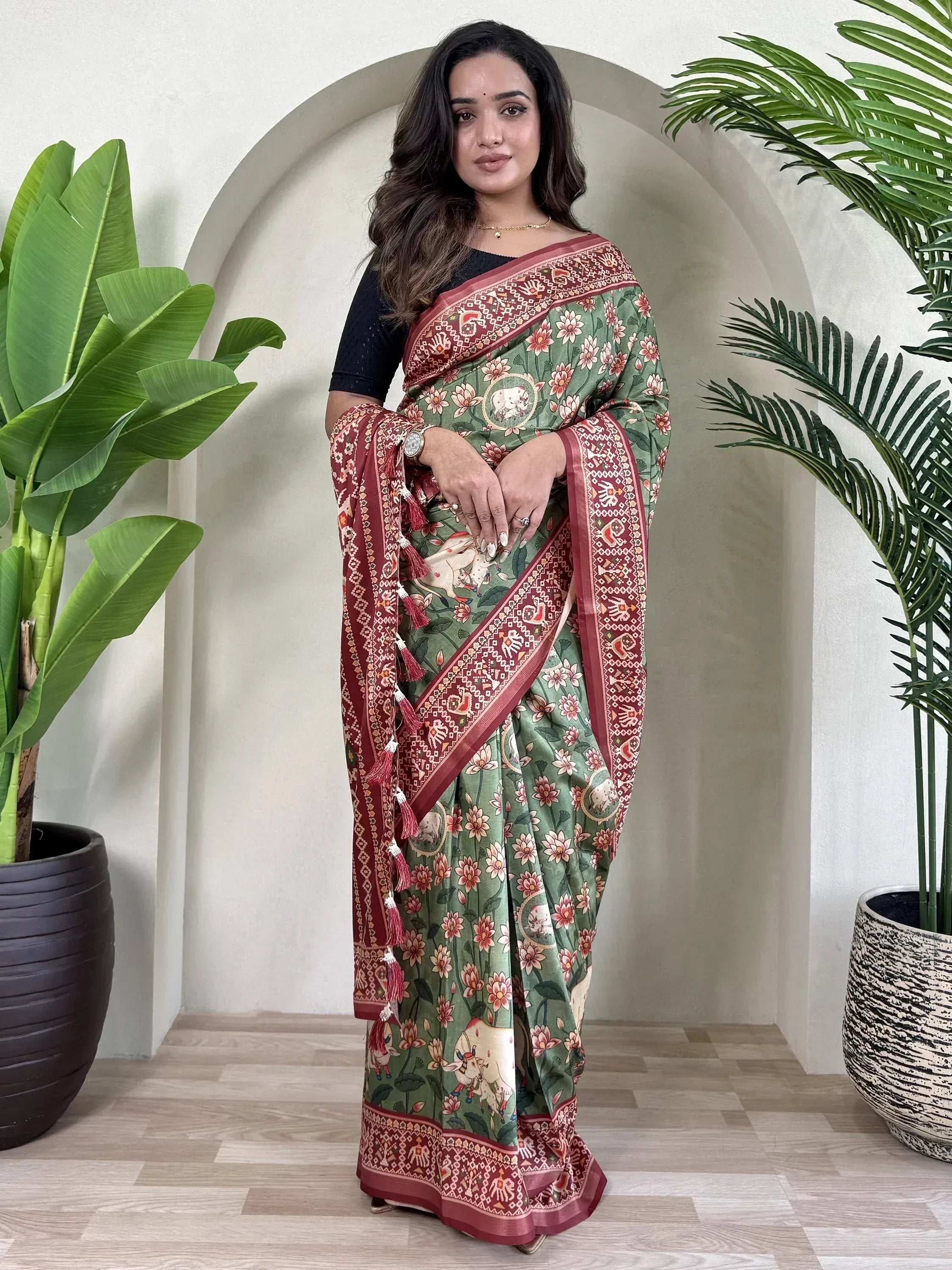 Woman in green floral saree with elephant print and red border, styled with black blouse for ethnic wear.