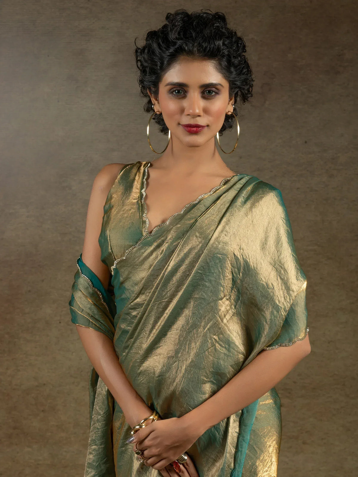 Woman in elegant green and gold saree with shimmering texture and delicate border, styled with hoop earrings.