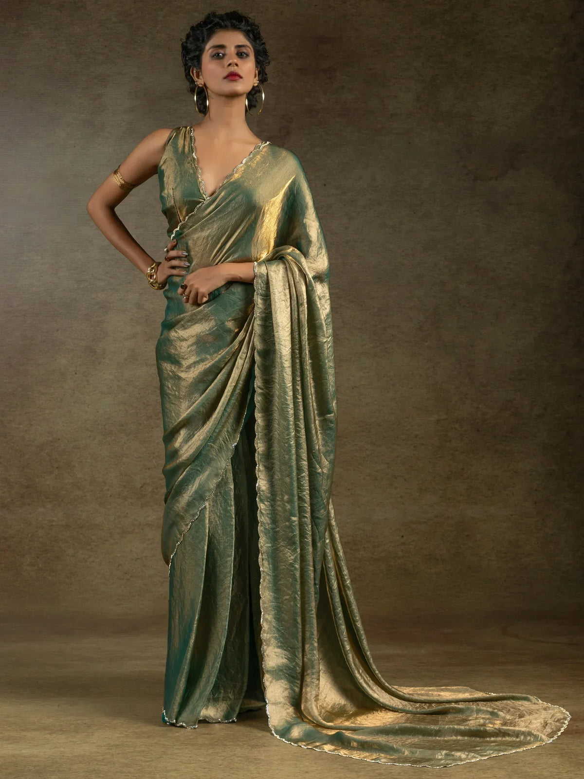 Elegant green and gold saree with shimmering texture and scalloped border, styled for festive occasions.