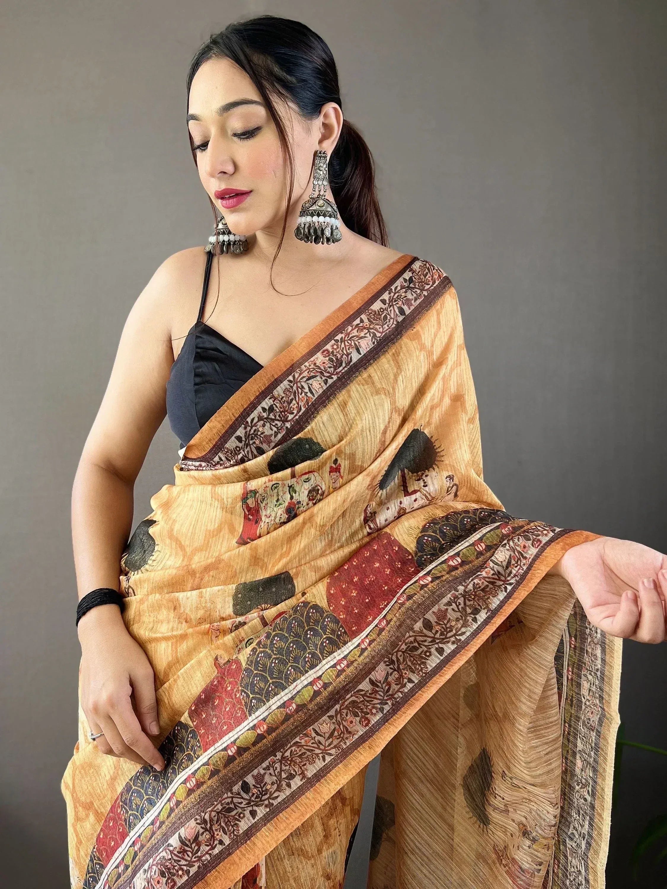 Woman in elegant printed saree with floral border, styled with black blouse and jhumka earrings for ethnic wear.