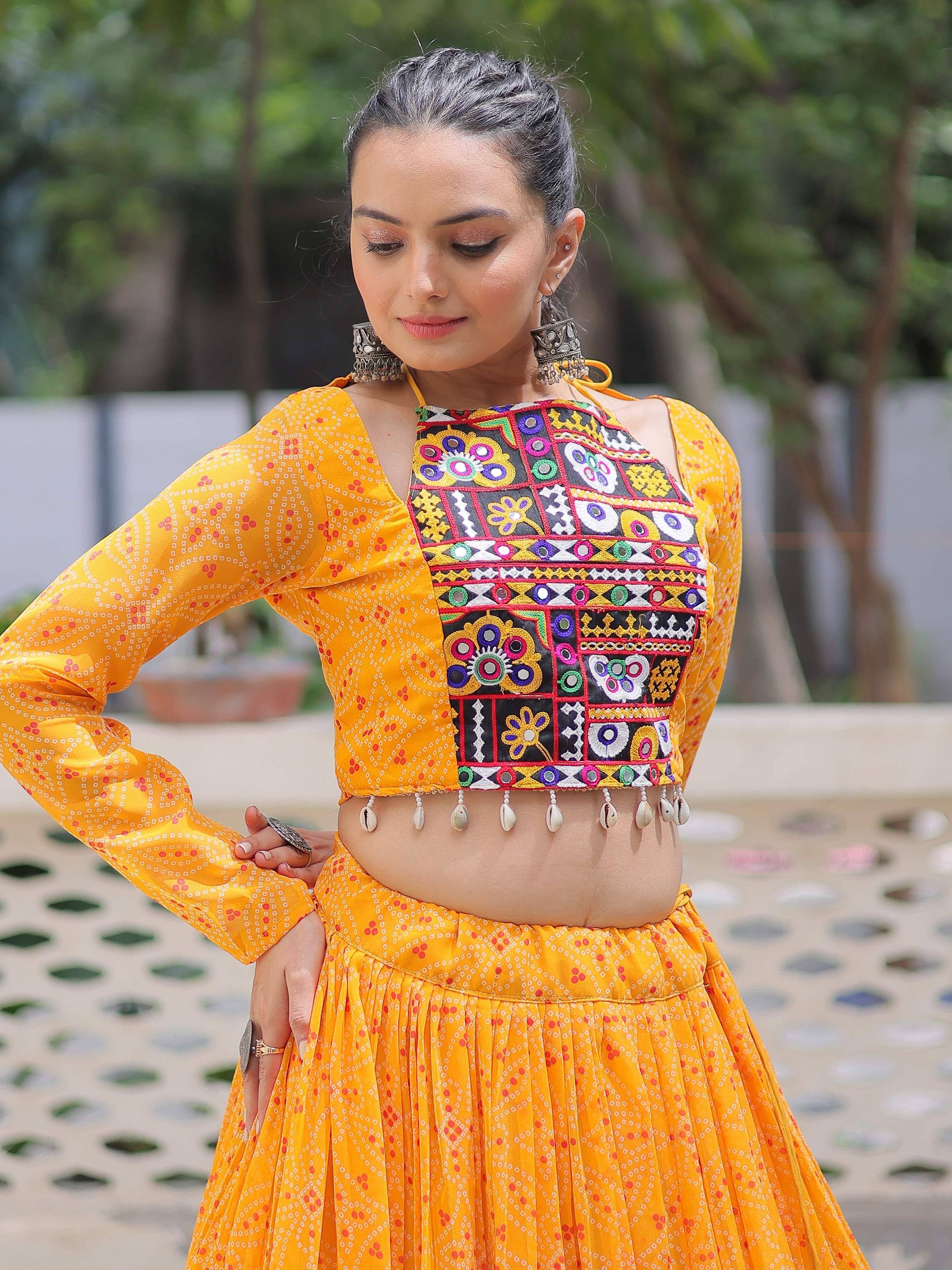 Vibrant yellow ethnic crop top with mirror work & shell tassels, paired with printed skirt for festive occasions