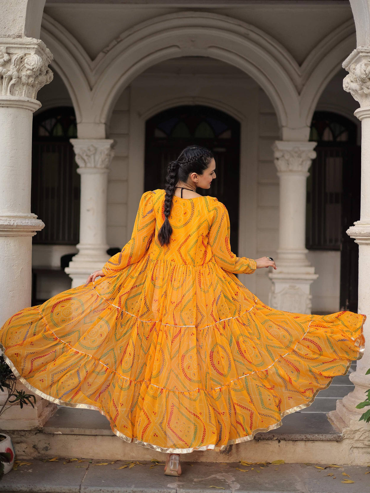 Woman twirling in vibrant yellow printed ethnic gown with tiered skirt, perfect for festive occasions.
