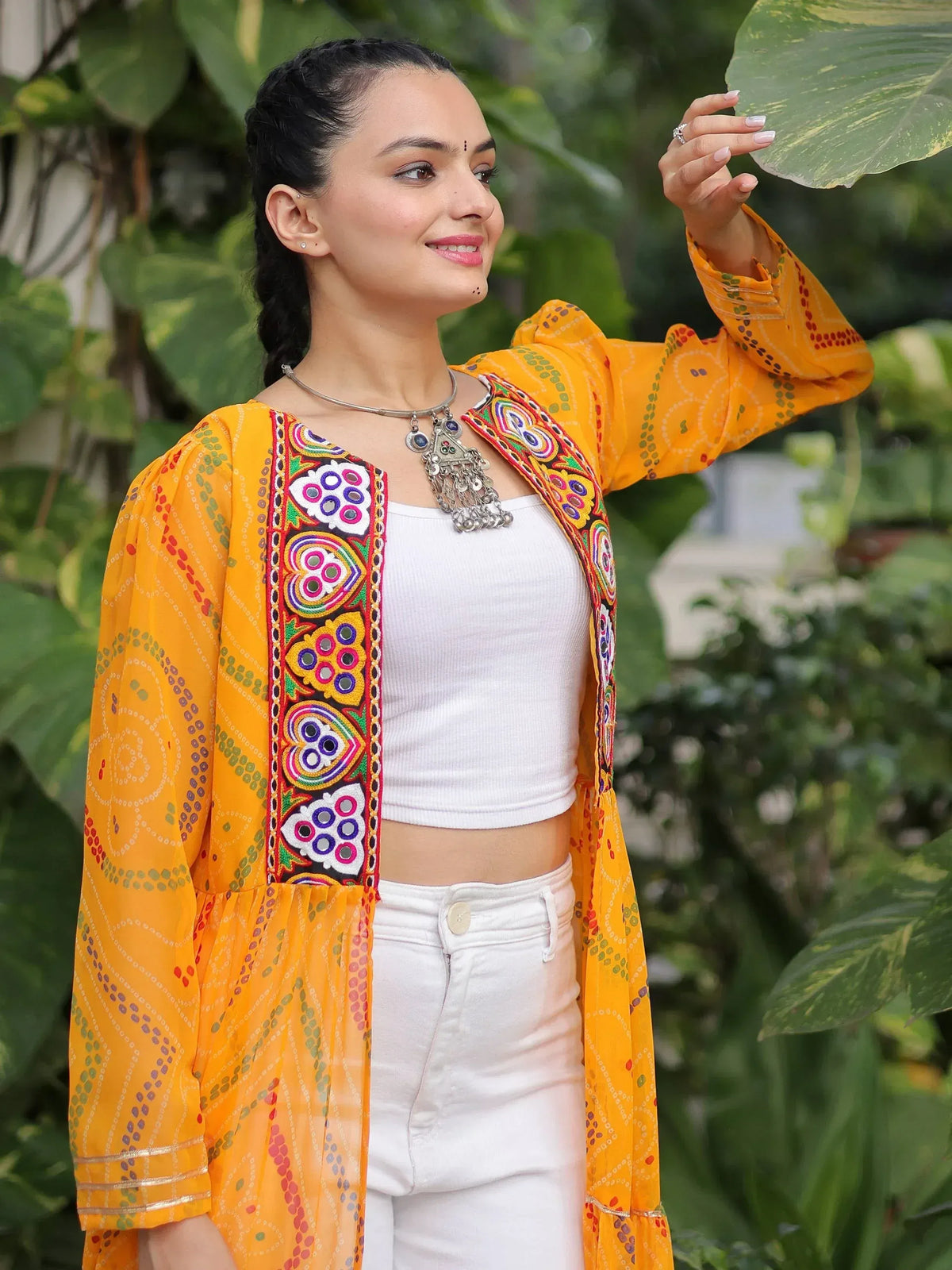 Woman in vibrant yellow embroidered ethnic jacket with mirror work, paired with white top and jeans, outdoors
