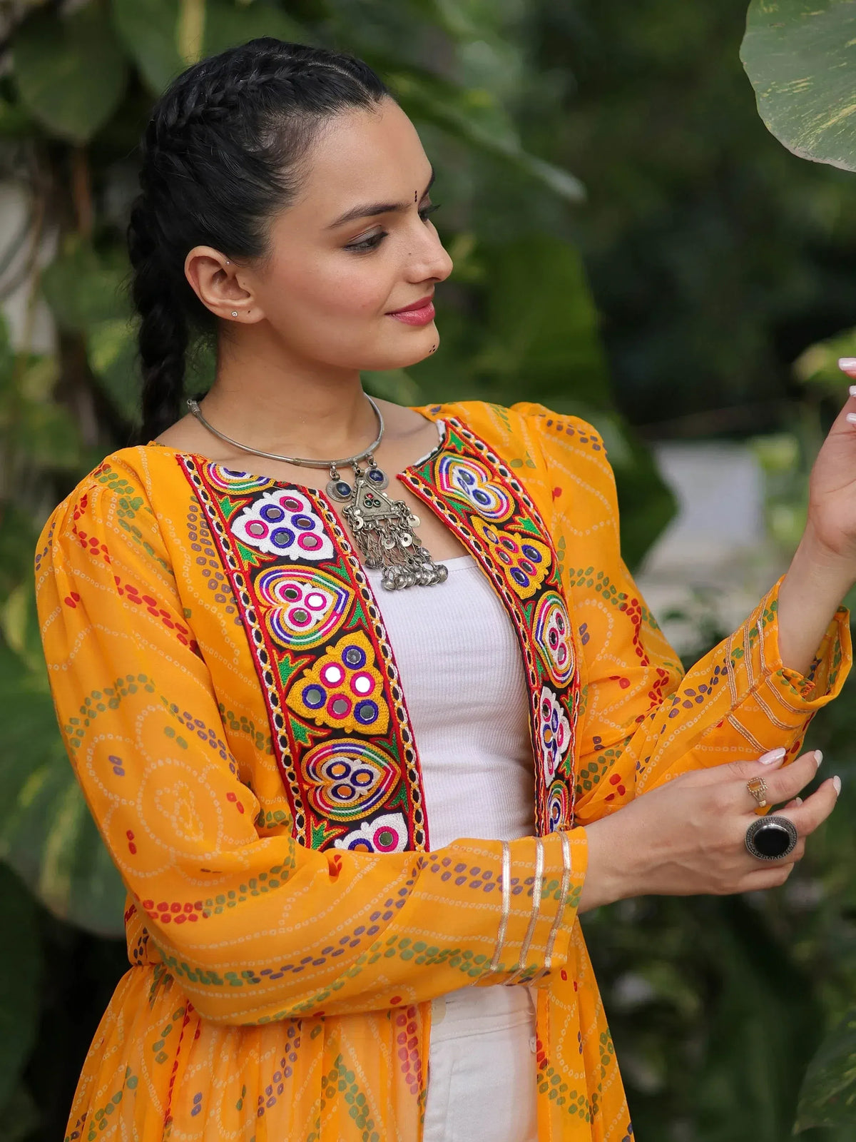 Woman in vibrant yellow embroidered ethnic kurta with mirror work, styled with silver jewelry and braided hair.