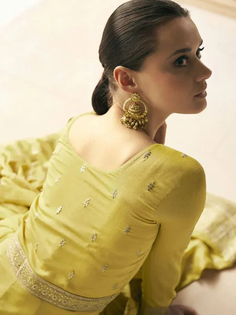 Woman in yellow ethnic gown with floral embroidery and gold jhumka earrings, showcasing Indian designer wear