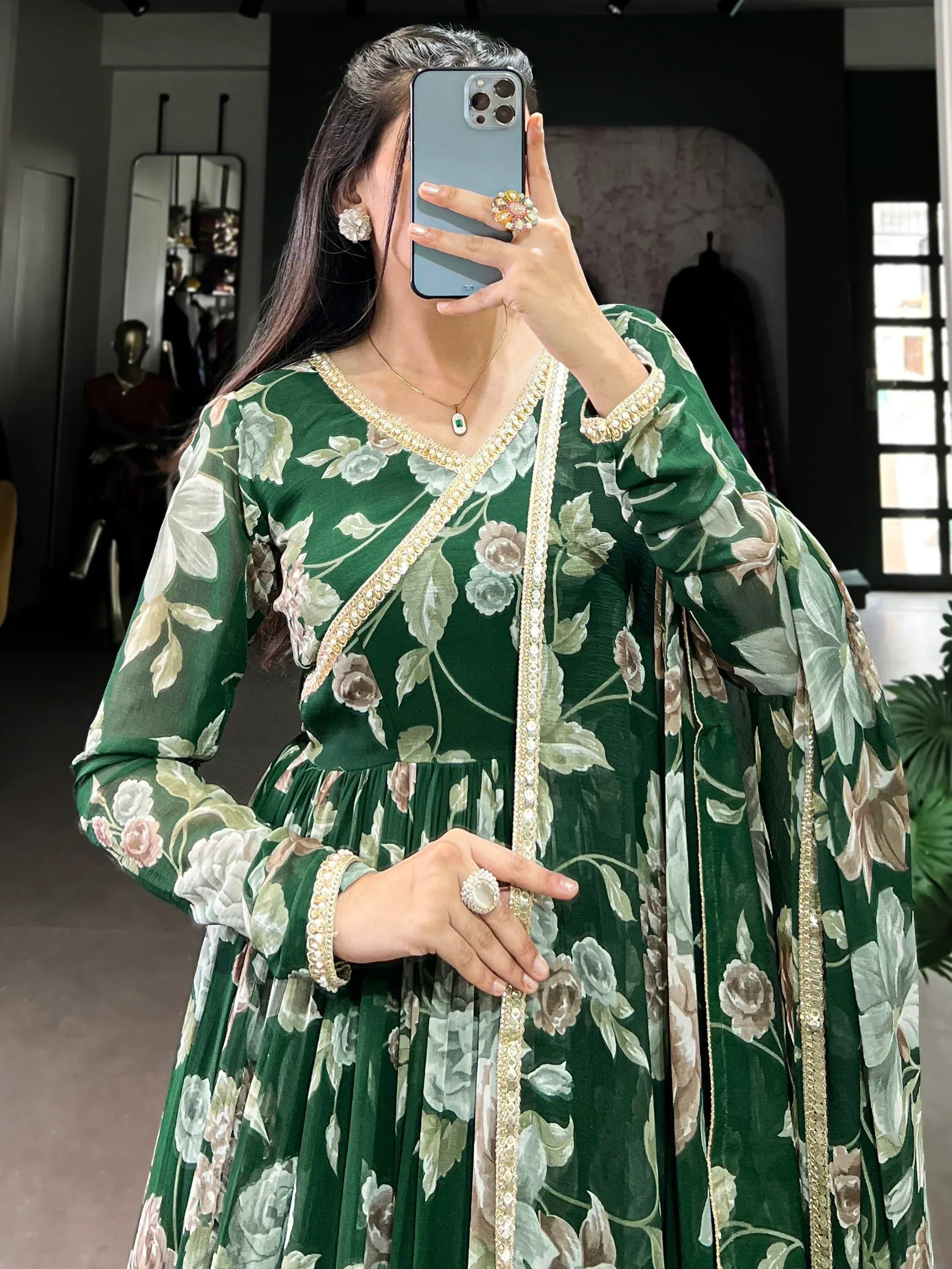 Woman wearing green floral ethnic gown with sheer sleeves and gold trim, taking mirror selfie