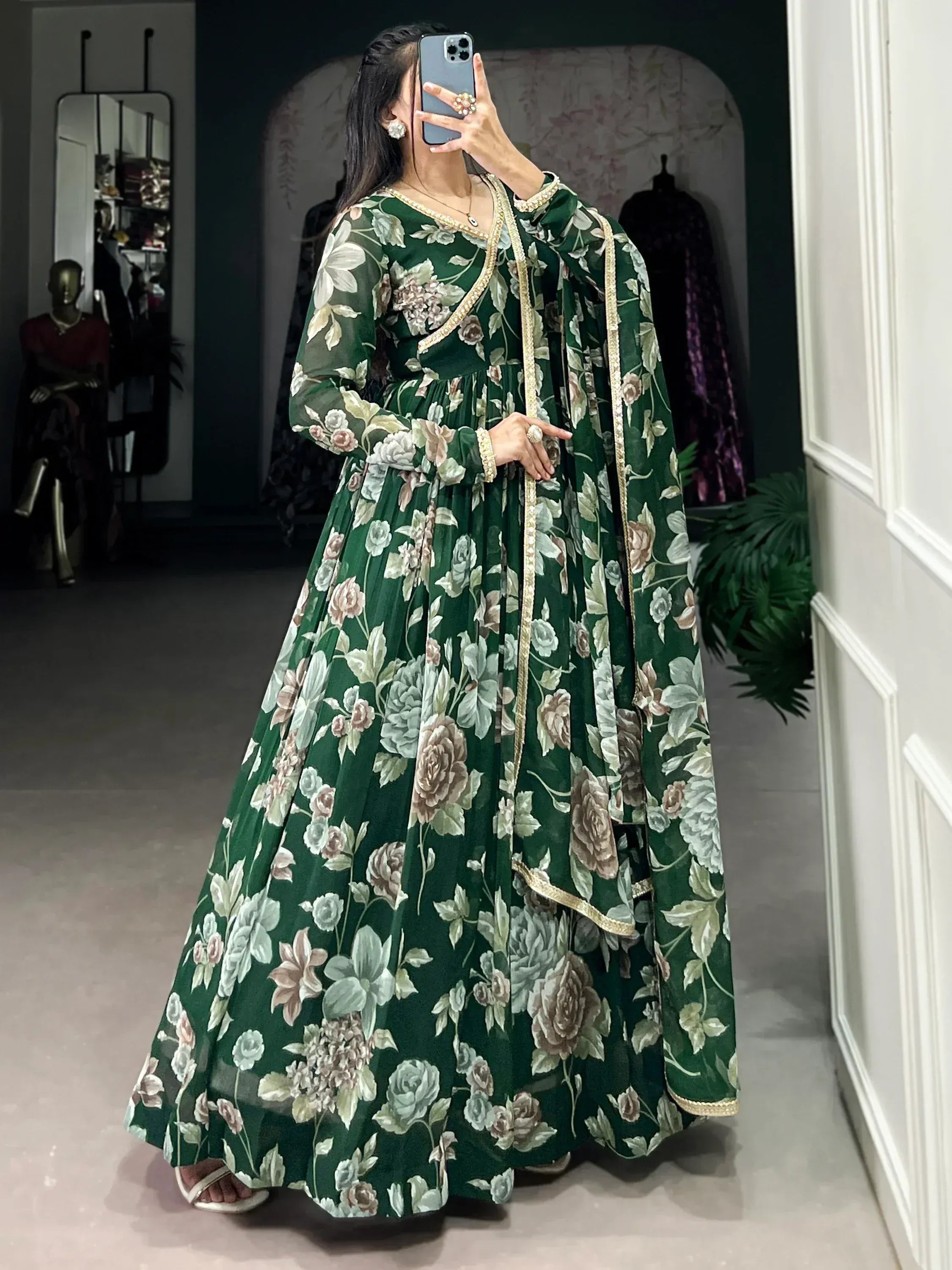Woman wearing green floral printed ethnic gown with dupatta, taking mirror selfie indoors