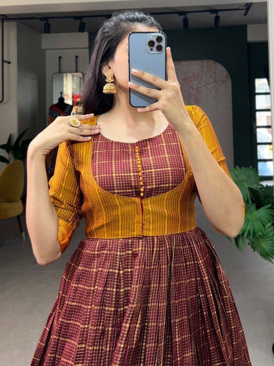 Maroon and mustard ethnic gown with checkered print, pleated skirt, and button front, styled with gold jhumka earrings.