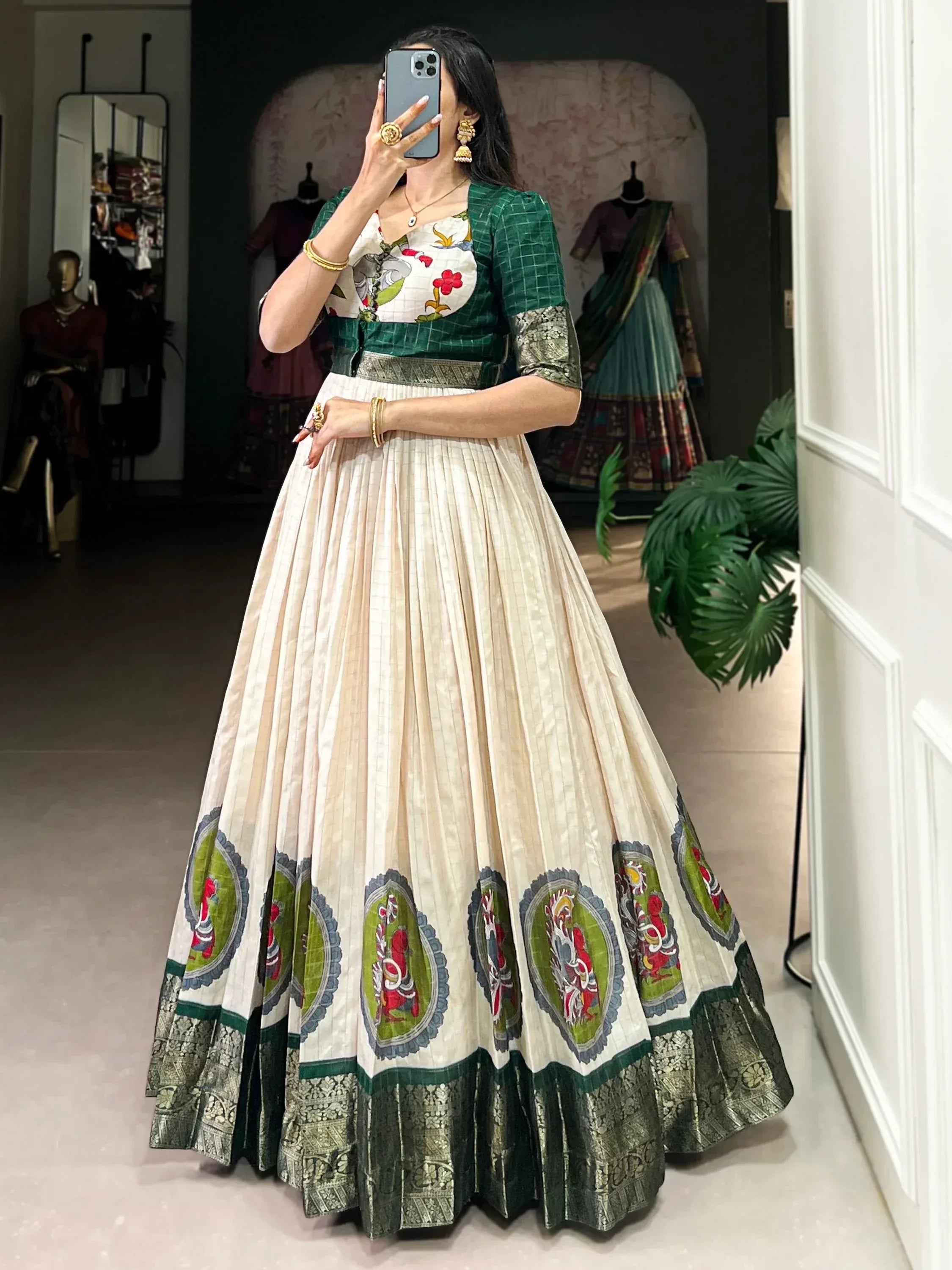 Woman wearing cream and green lehenga choli with floral and deity motifs, traditional jewelry