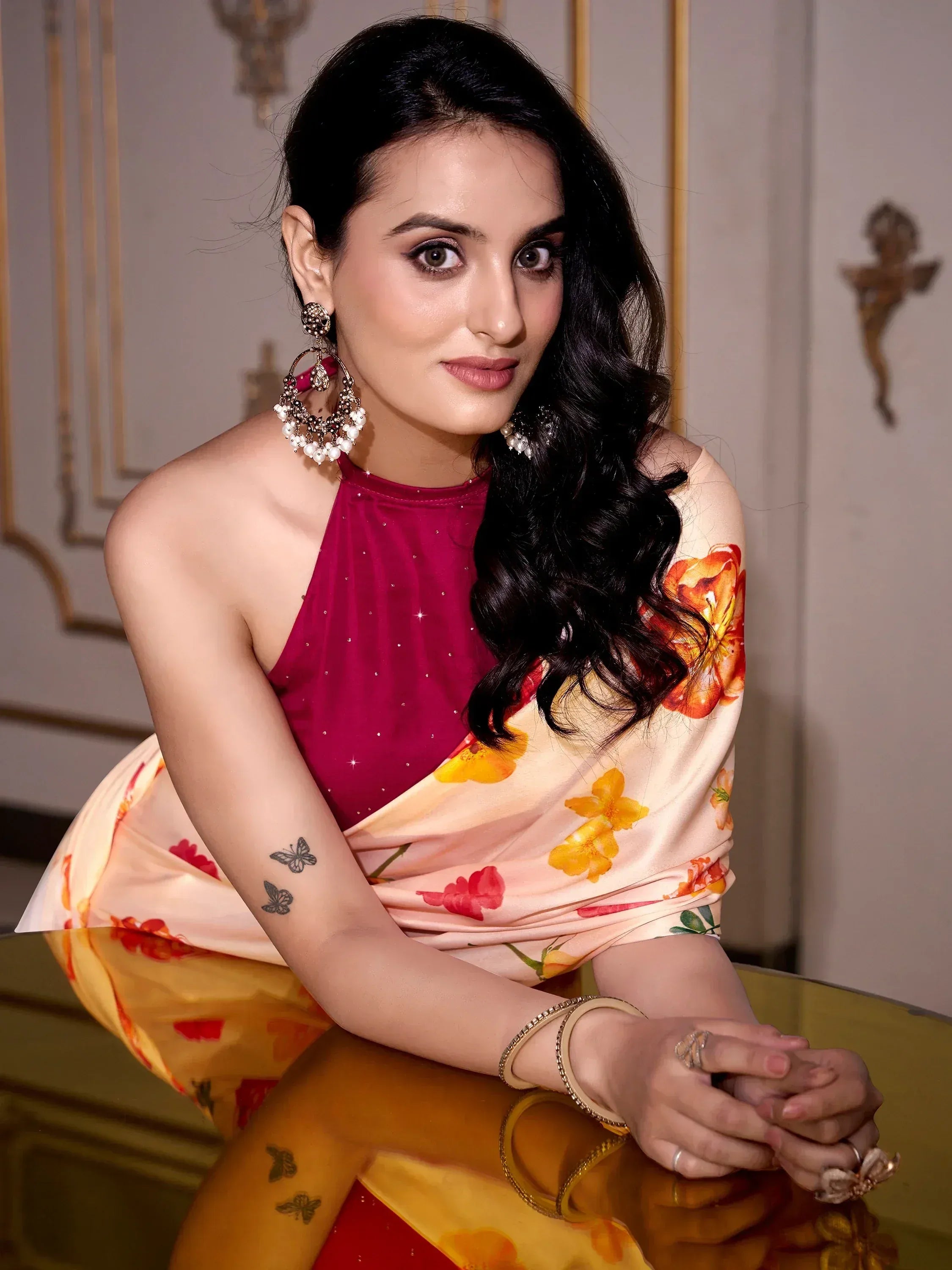 Woman in floral saree with maroon blouse, statement earrings, and butterfly tattoos, styled for ethnic wear.
