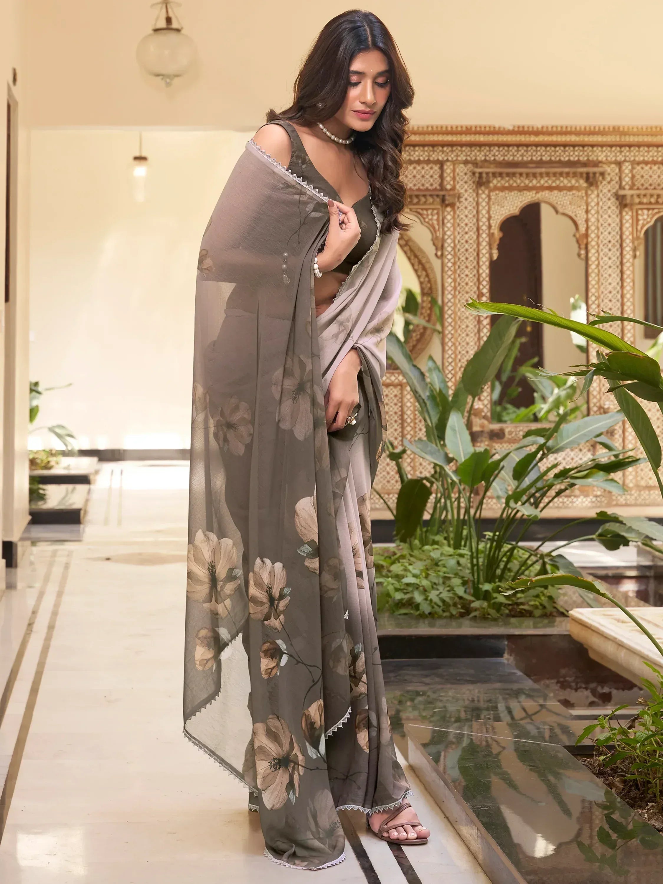 Woman in grey floral print saree with lace trim, styled with pearl necklace in elegant indoor setting