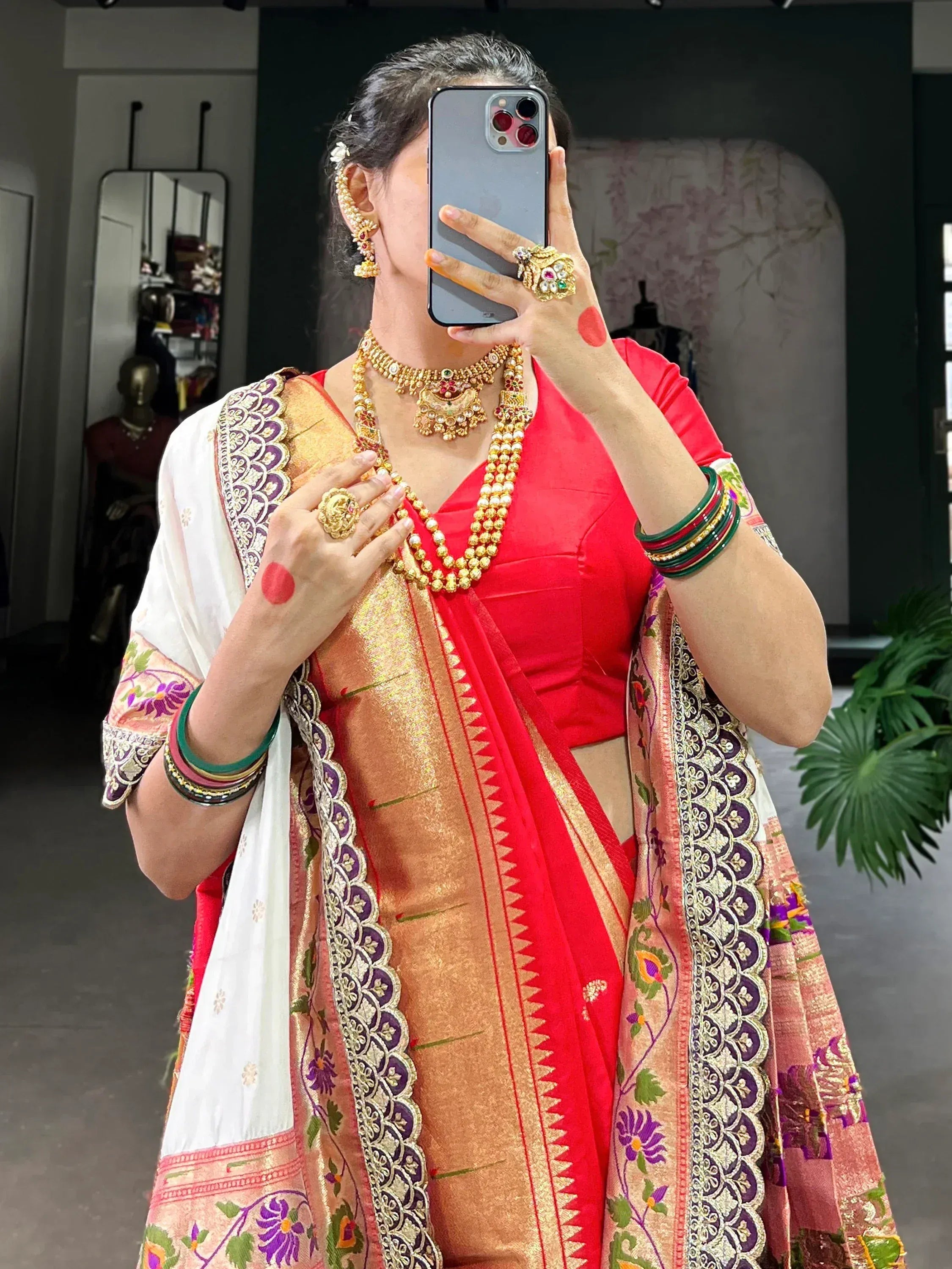 Woman in red and gold saree with intricate embroidery and traditional jewelry, taking mirror selfie.