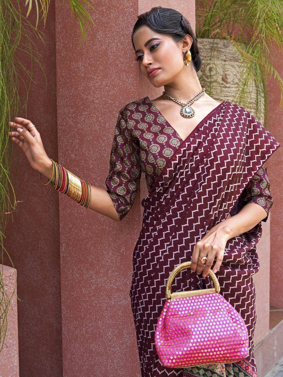 Woman in maroon printed saree with gold jewelry and pink sequin handbag, ethnic Indian wear