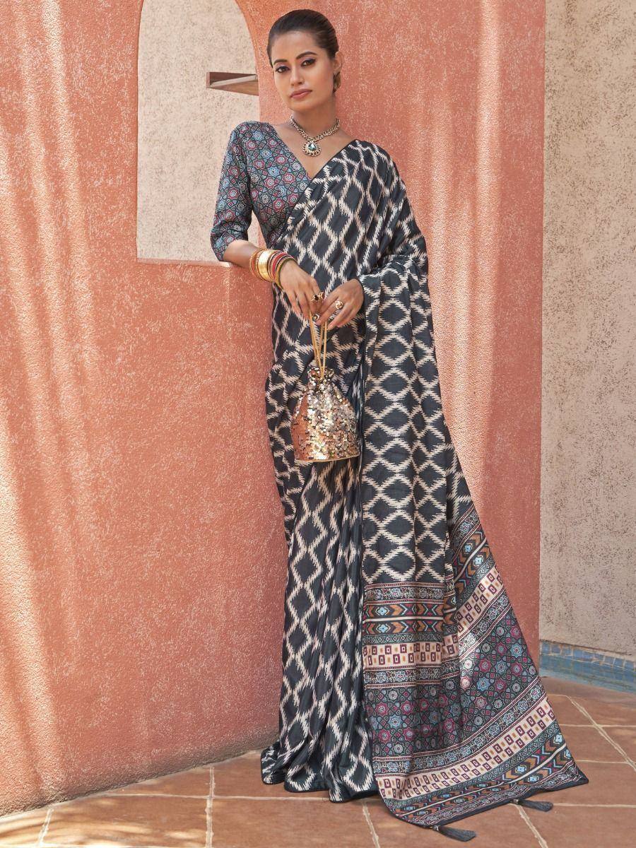 Woman in black and white ikat print saree with colorful border, paired with patterned blouse and gold accessories
