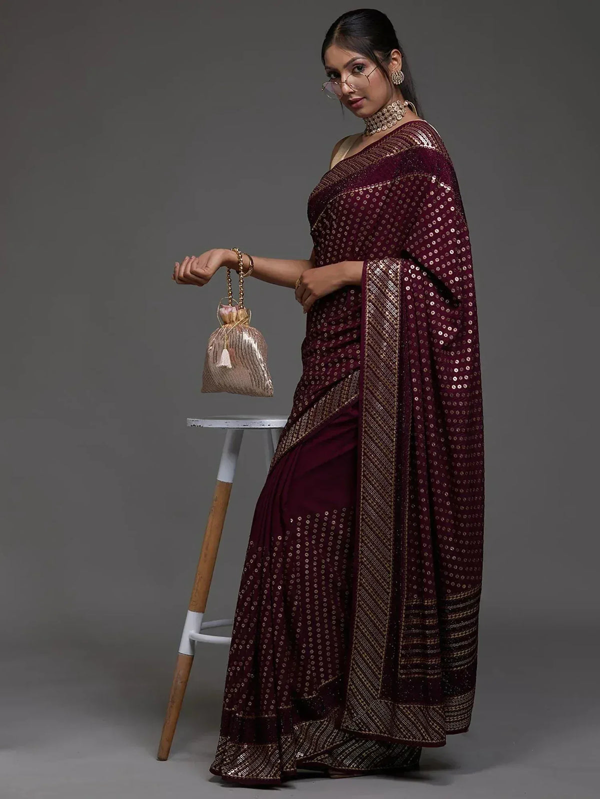 Maroon sequin saree with gold border, styled with statement jewelry and potli bag for ethnic occasions