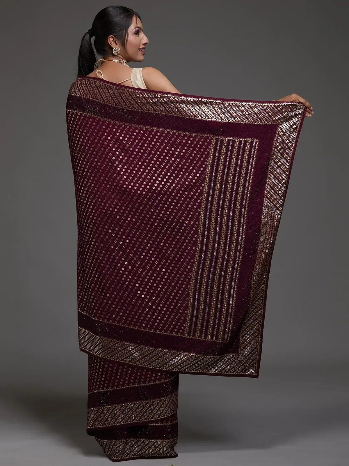 Woman showcasing maroon saree with gold sequin detailing and border, ideal for ethnic occasions.