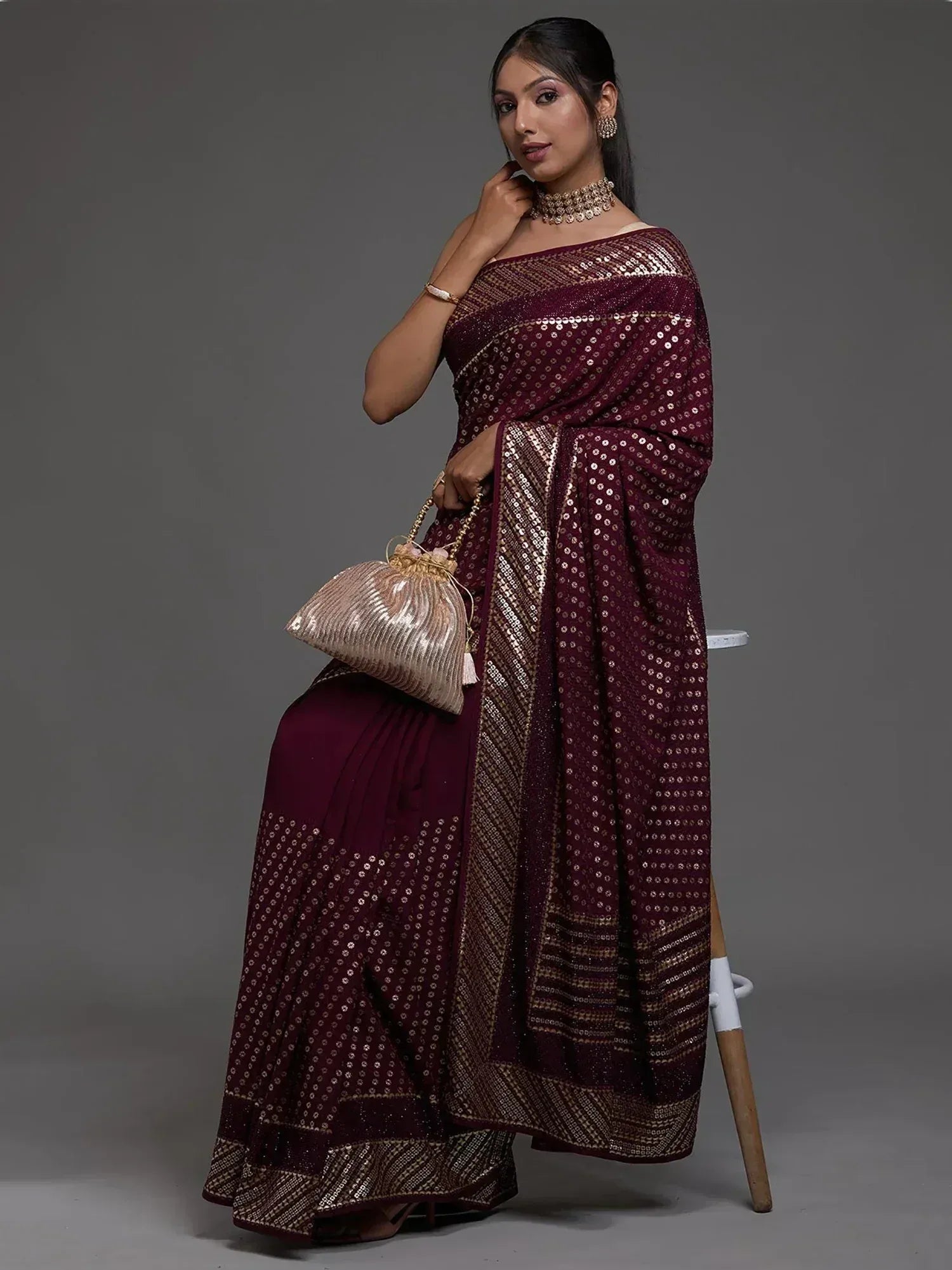 Elegant maroon saree with gold sequin work, paired with statement jewelry and clutch, perfect for Indian ethnic occasions.
