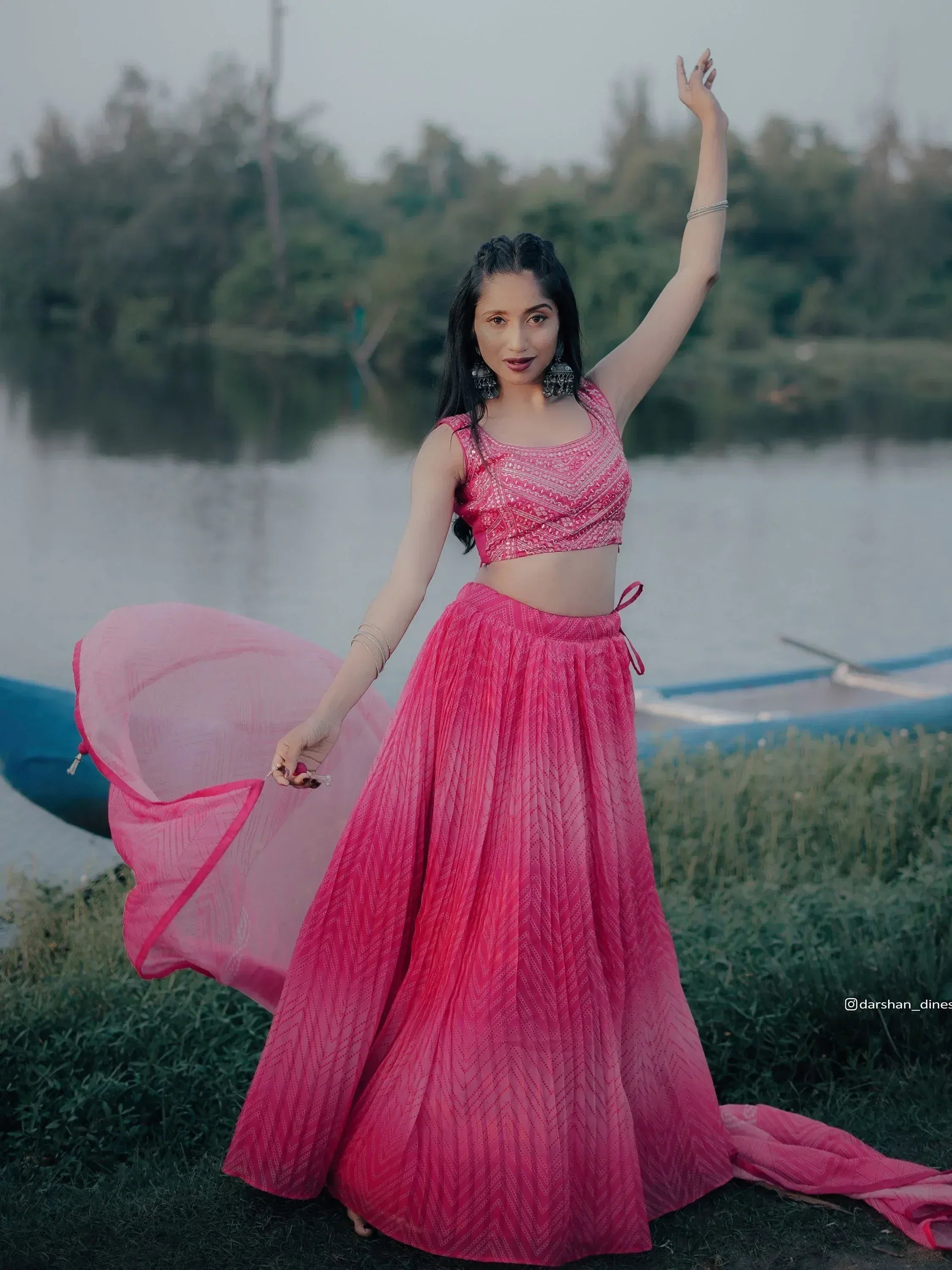 Pink ethnic lehenga choli with geometric patterns, worn by a woman near a lakeside