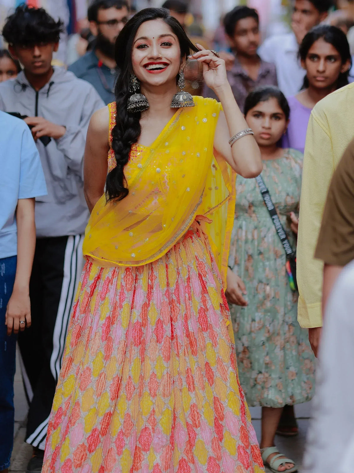 Woman in vibrant yellow and pink designer lehenga choli with jhumka earrings, perfect for Indian ethnic wear occasions.