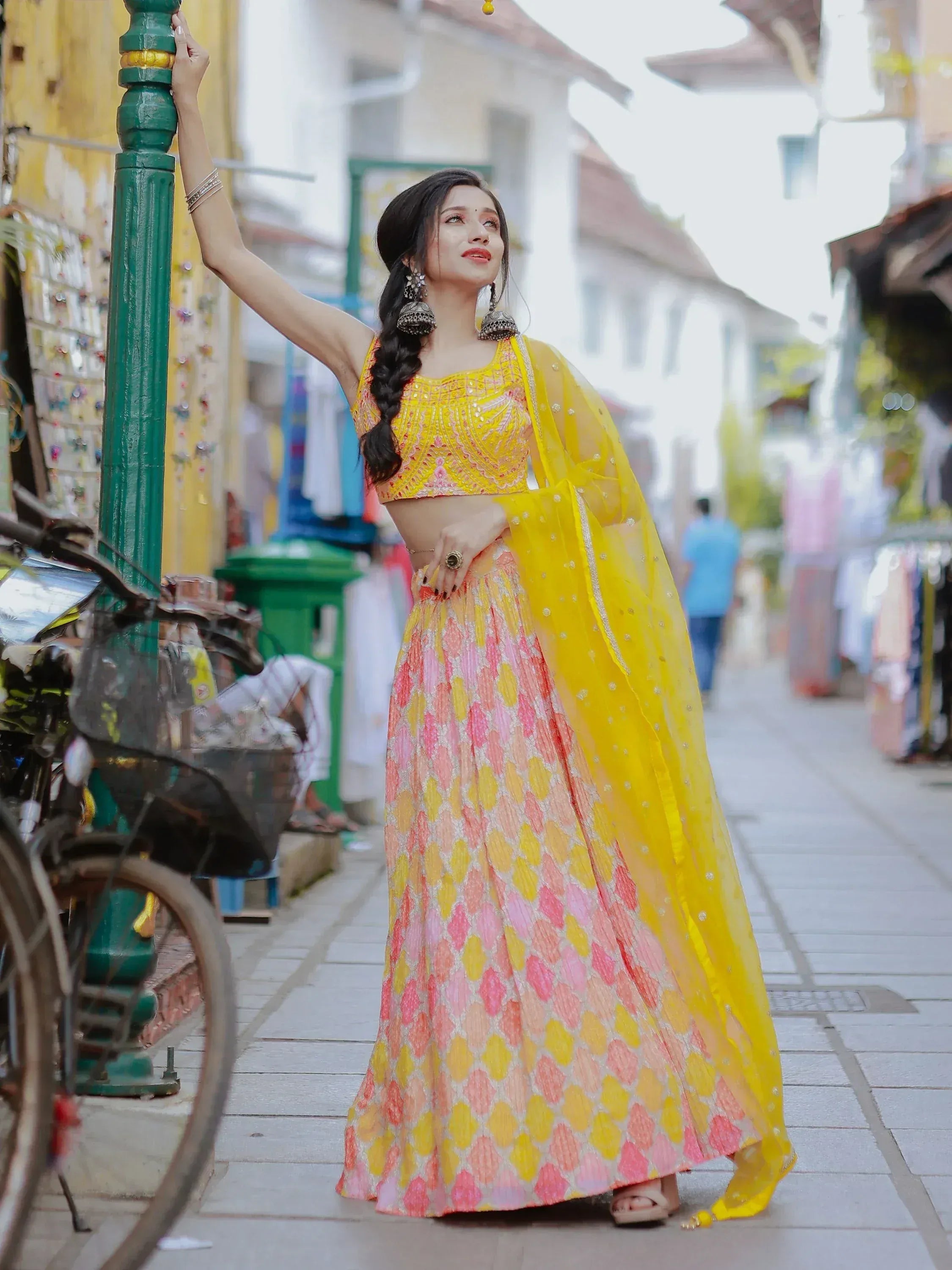 Woman in vibrant yellow and pink lehenga choli with dupatta, posing on a colorful street