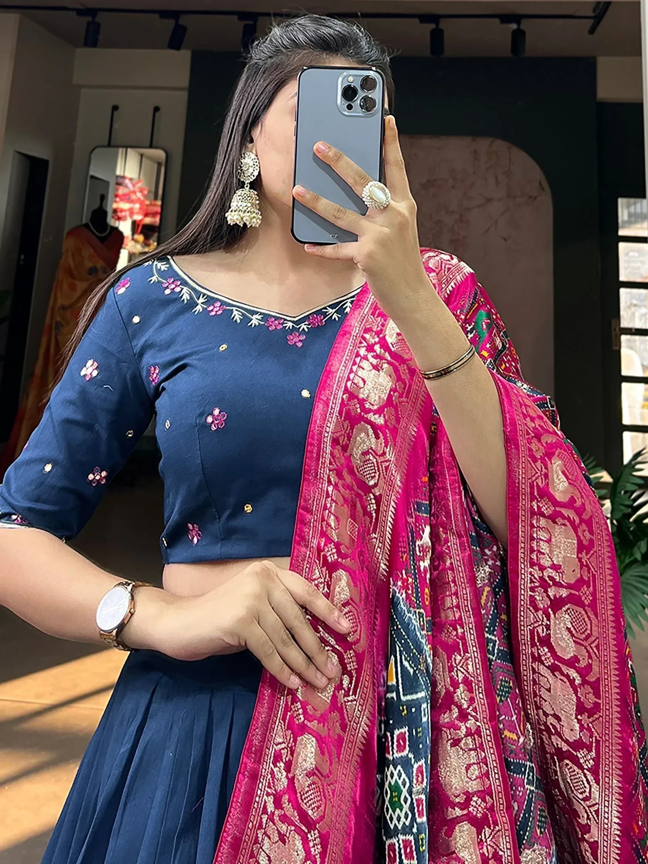 Woman in navy blue embroidered crop top and pleated skirt with pink printed dupatta, taking mirror selfie