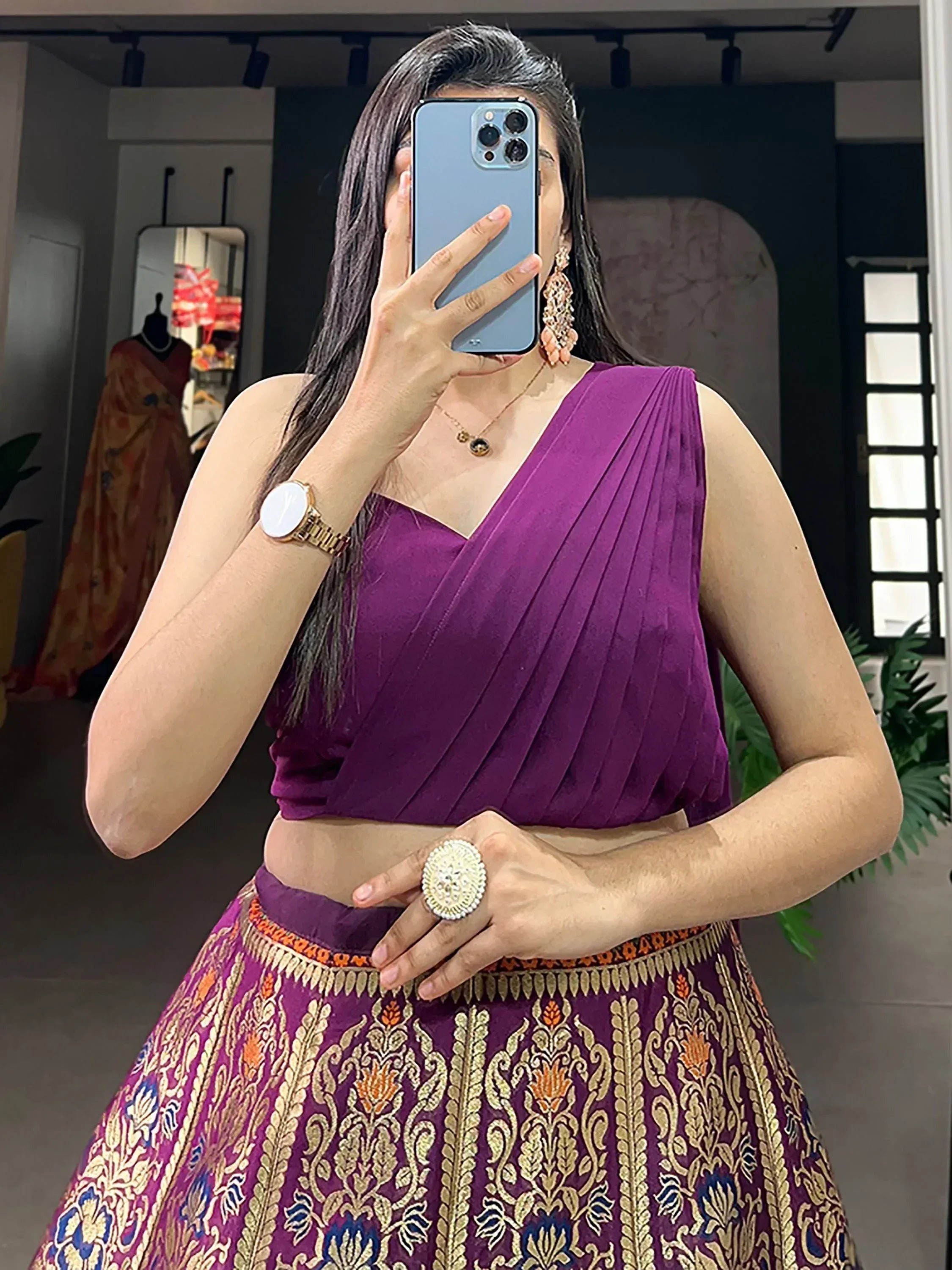 Woman in purple pleated lehenga choli with gold embroidery, taking mirror selfie in boutique