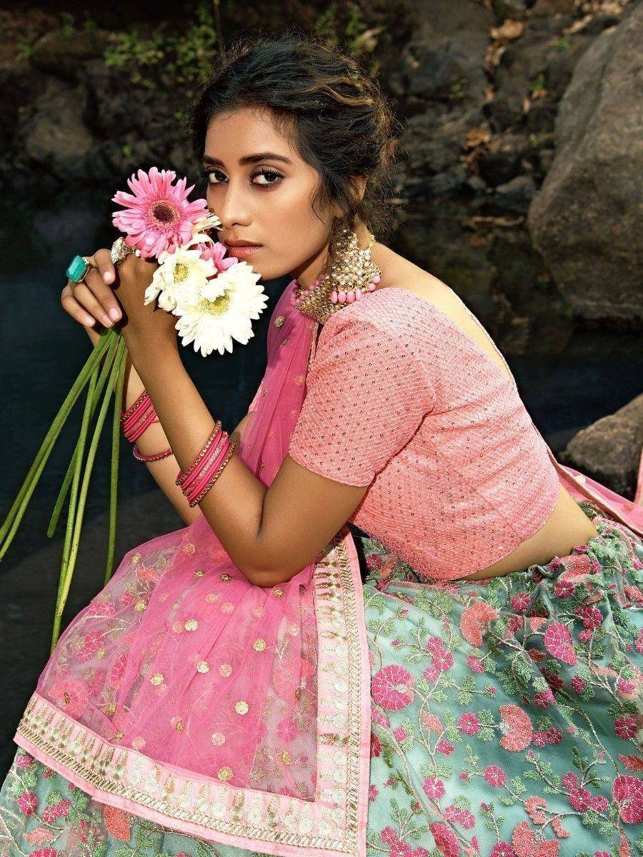 Woman in pink and green floral lehenga choli holding flowers, ethnic Indian wear